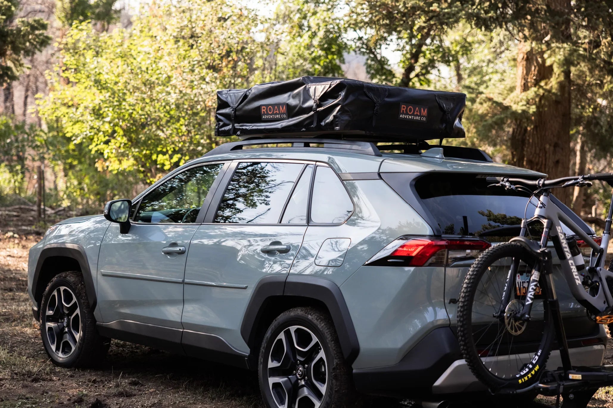 SUV with rooftop tent and mountain bike in a forest, ideal for overlanding and camping gear