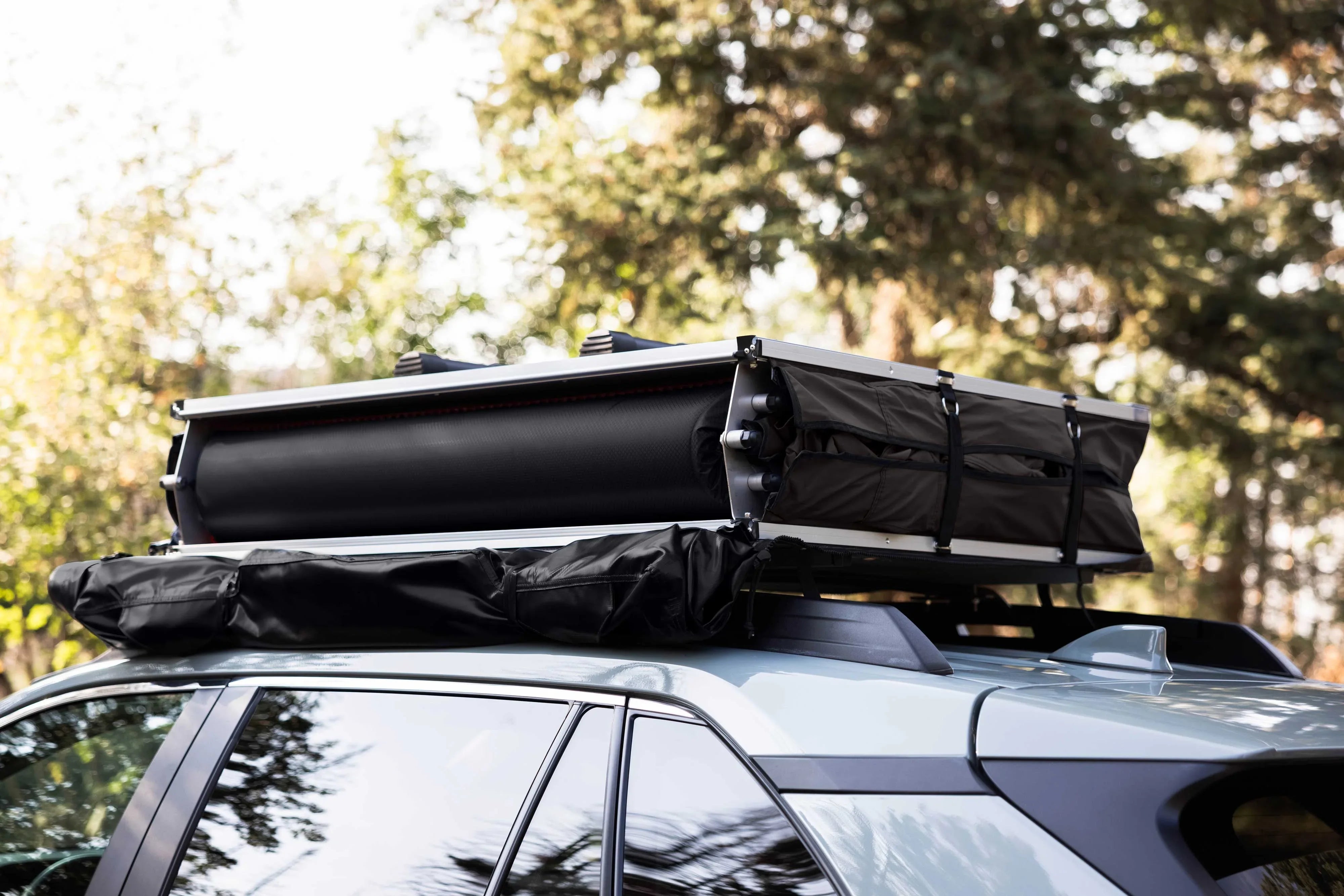 Overland rooftop tent and awning mounted on SUV roof rack in outdoor setting