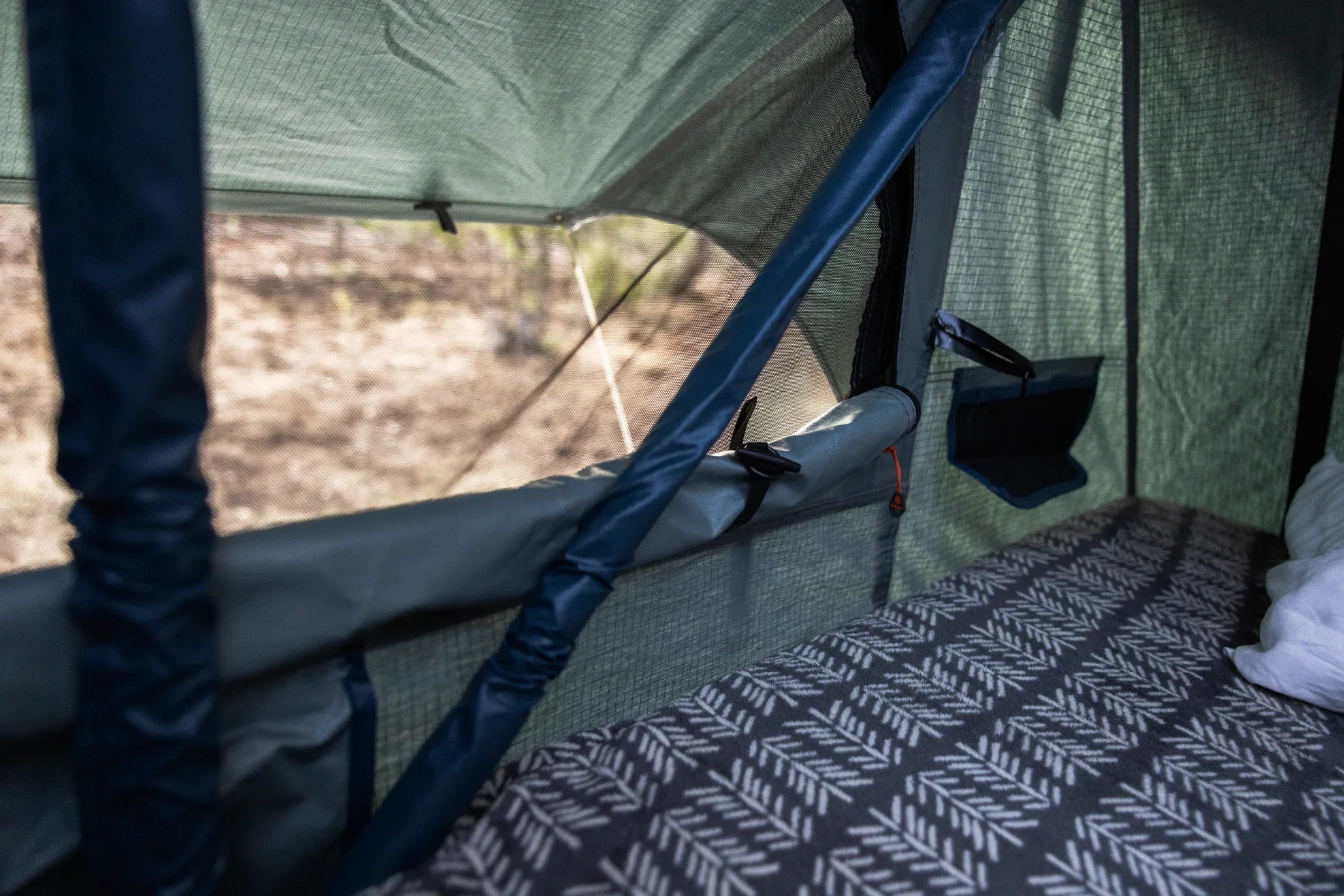 Interior of an overlanding rooftop tent with mesh windows and patterned sleeping pad.