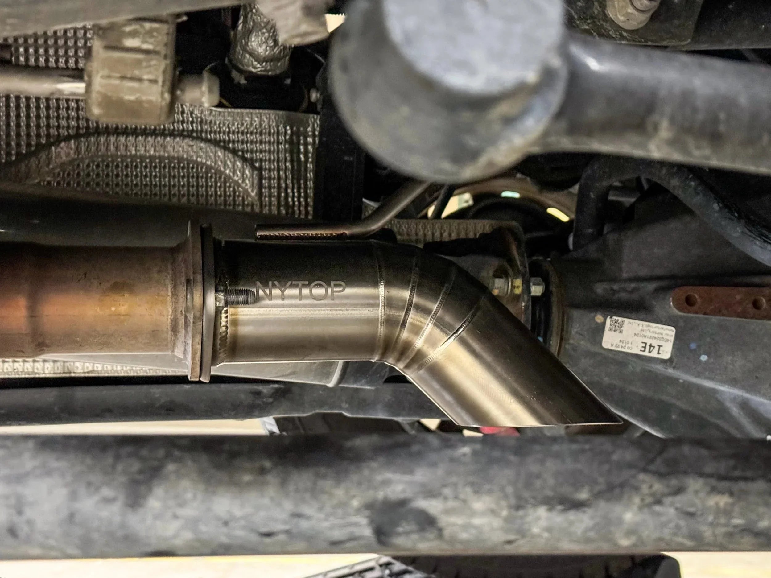 Aftermarket stainless steel exhaust tip installed on off-road vehicle undercarriage