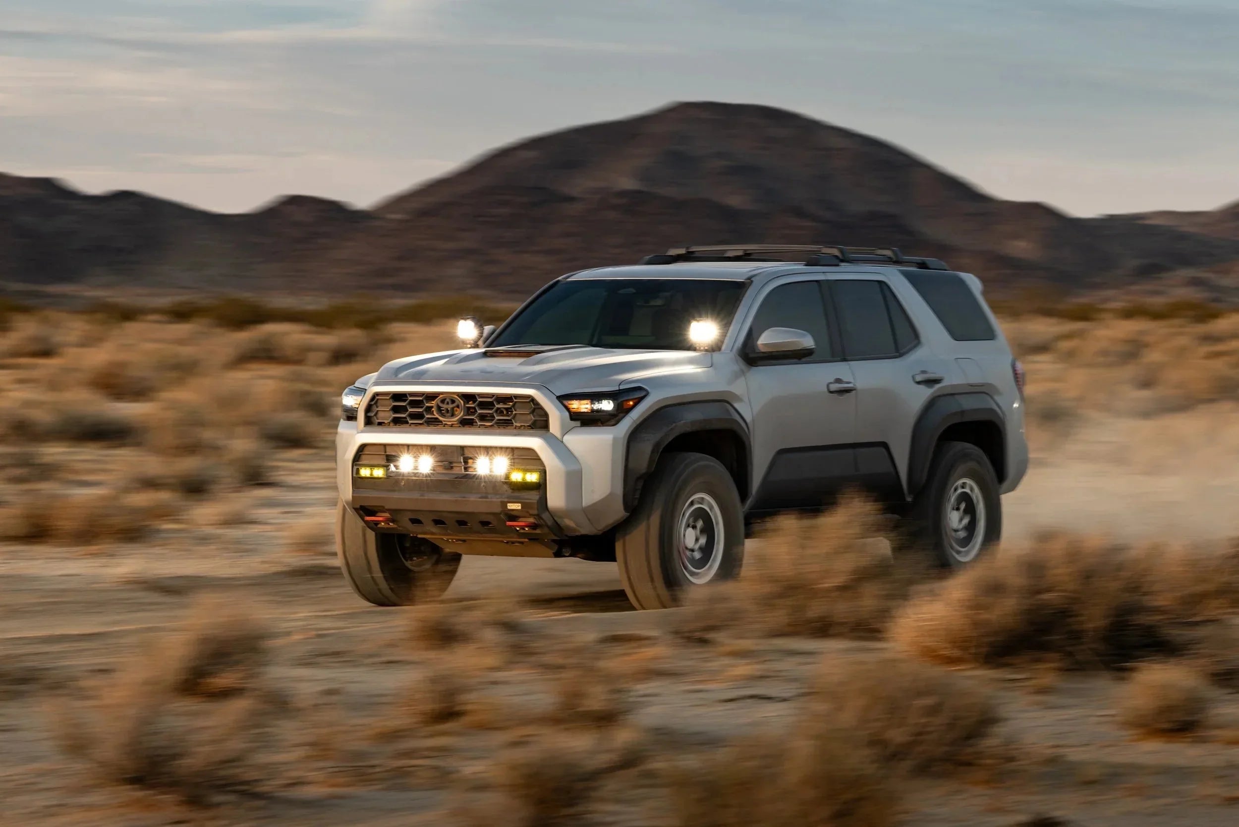 Toyota 4Runner SUV with off-road lights driving in desert landscape with mountains