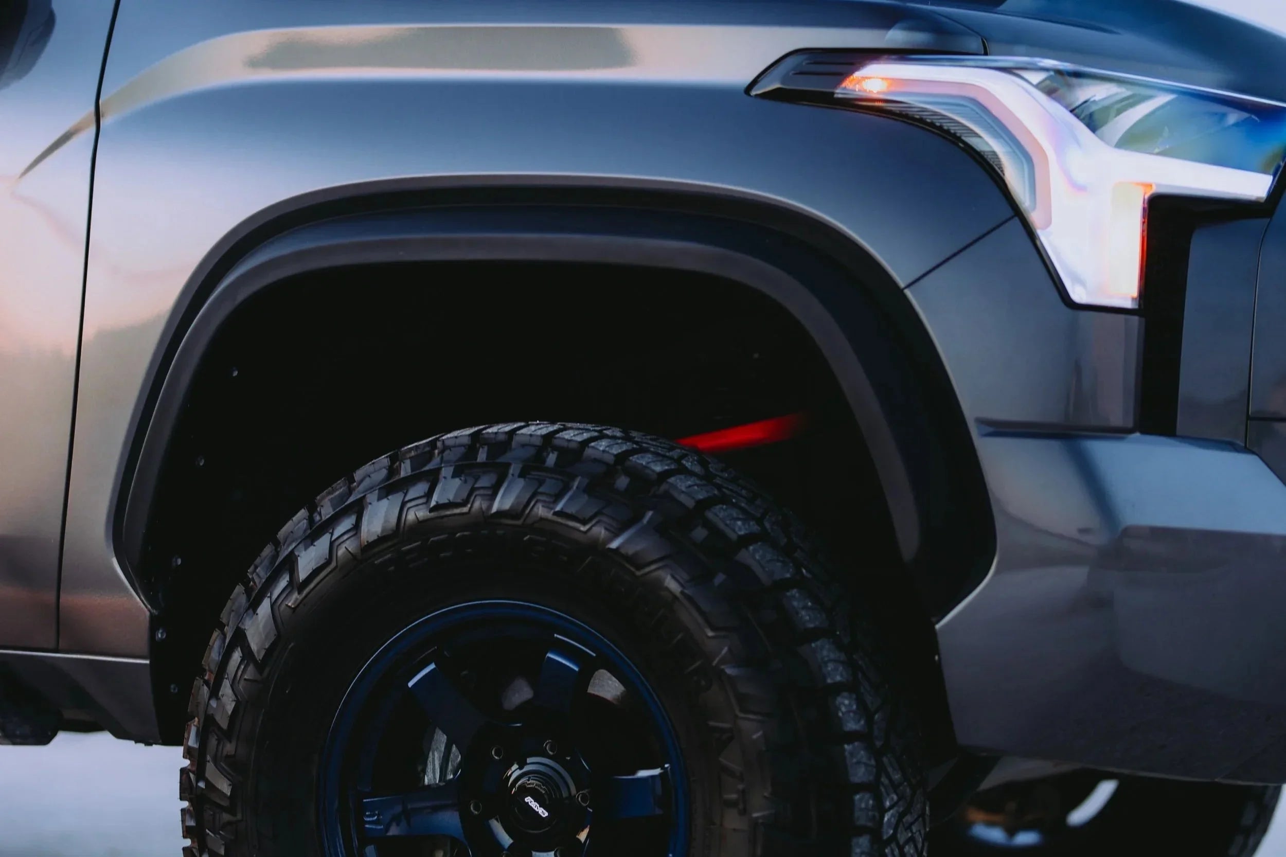 Close-up of off-road tire and custom fender on a rugged Toyota truck, outdoor lighting