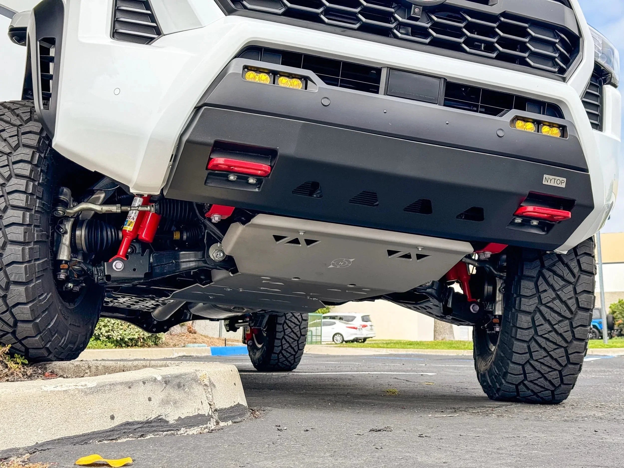 Close-up of off-road vehicle front skid plate and suspension, rugged tires, and bumper accessories.