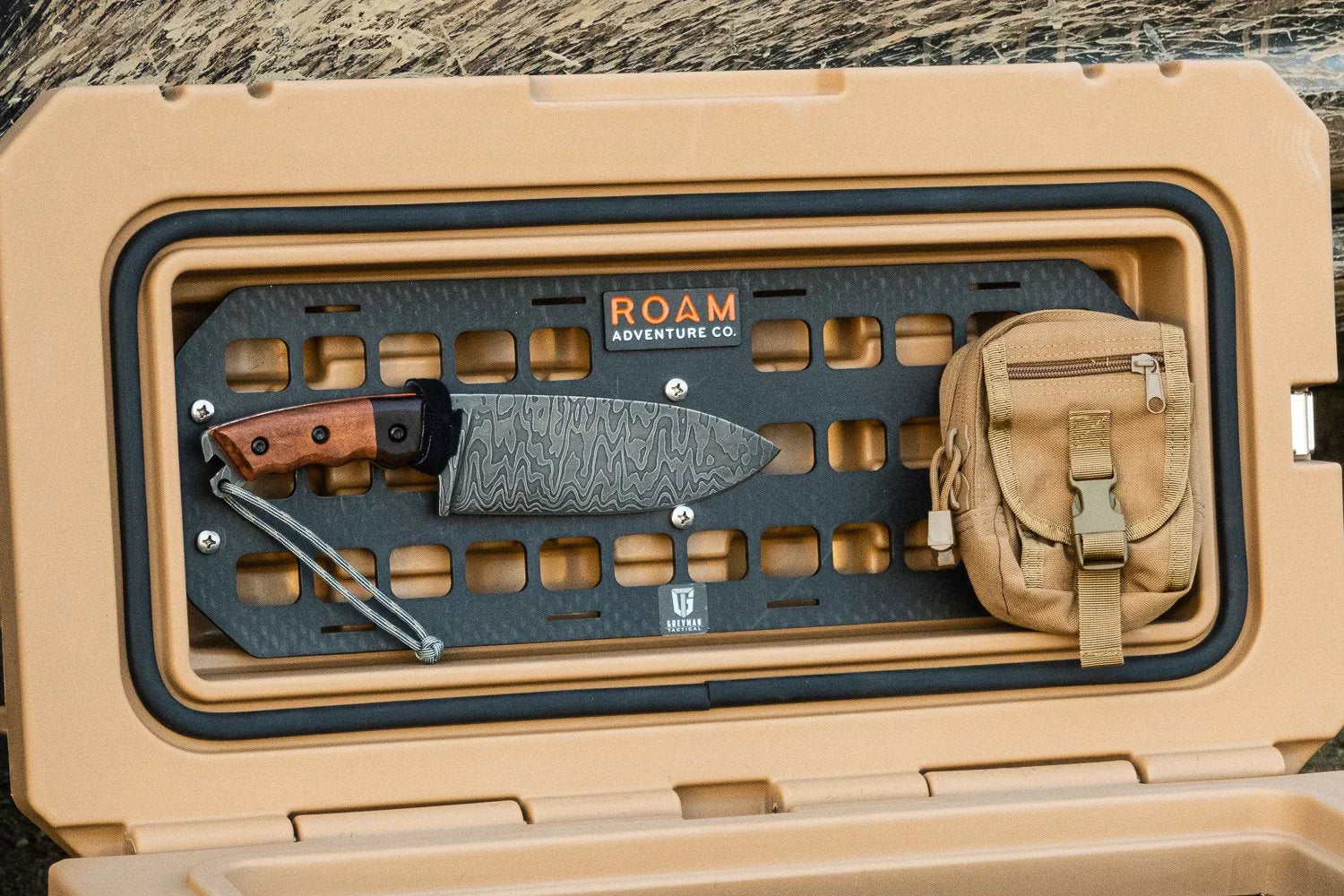 Overland gear: tactical knife and tan pouch on storage box MOLLE panel, outdoor setting