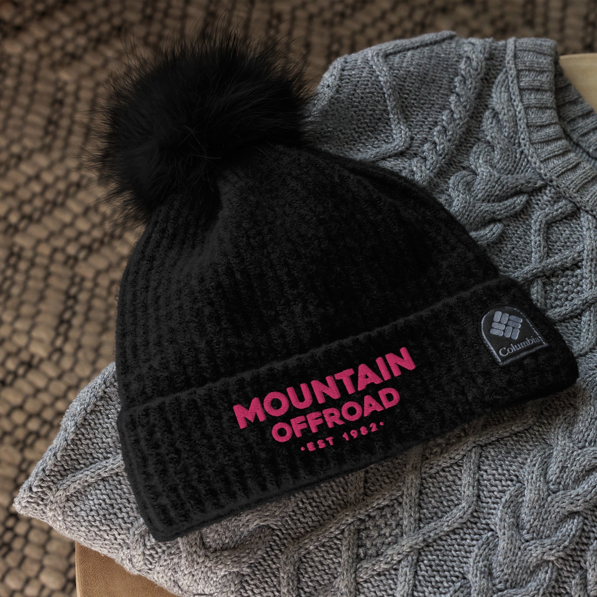 Black ladies' beanie with faux fur pom, 'Mountain Offroad' text, on a gray knit sweater