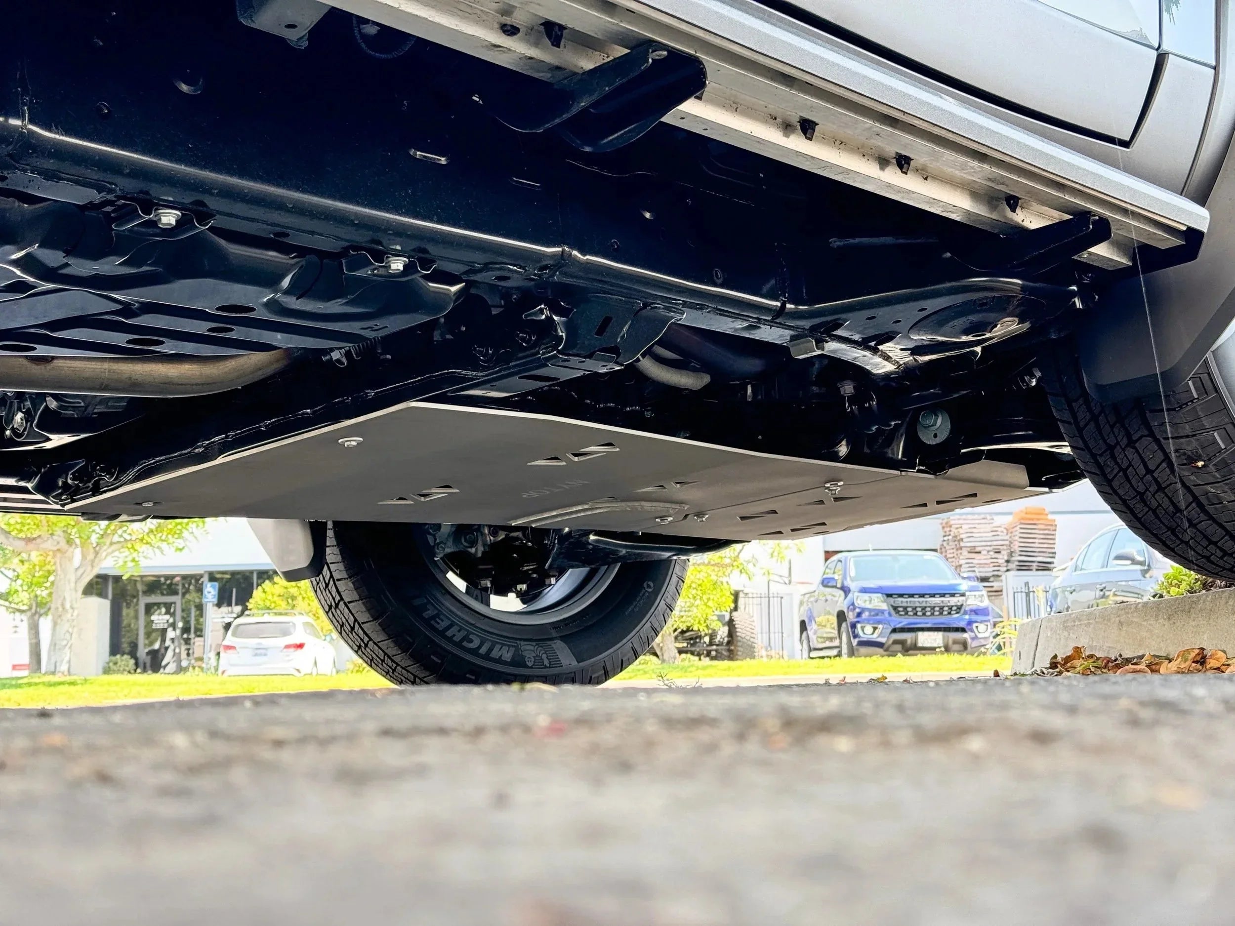 Underbody view of a vehicle with off-road skid plate and Michelin tire in a parking lot