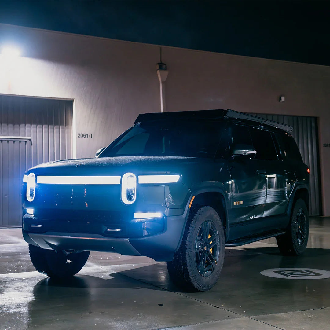 Rivian SUV with illuminated LED headlights and rugged tires parked at night, overlanding vehicle