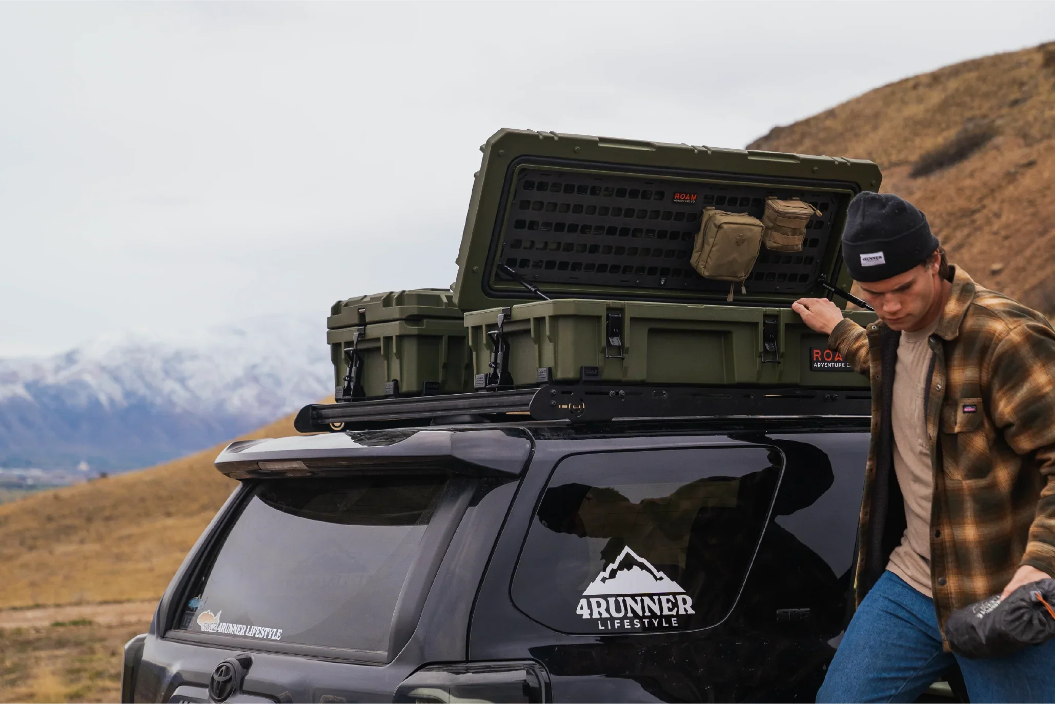 Man with roof storage boxes on Toyota 4Runner SUV, overlanding gear, outdoor mountain setting
