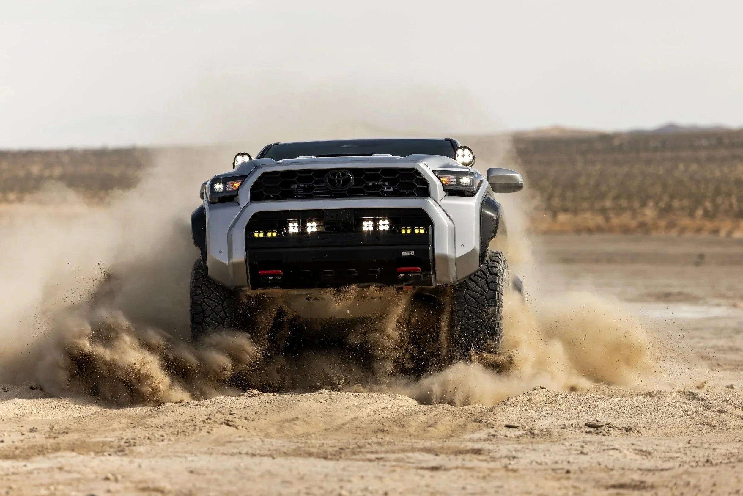 Toyota Tacoma off-road truck driving through desert sand with custom lights and rugged tires