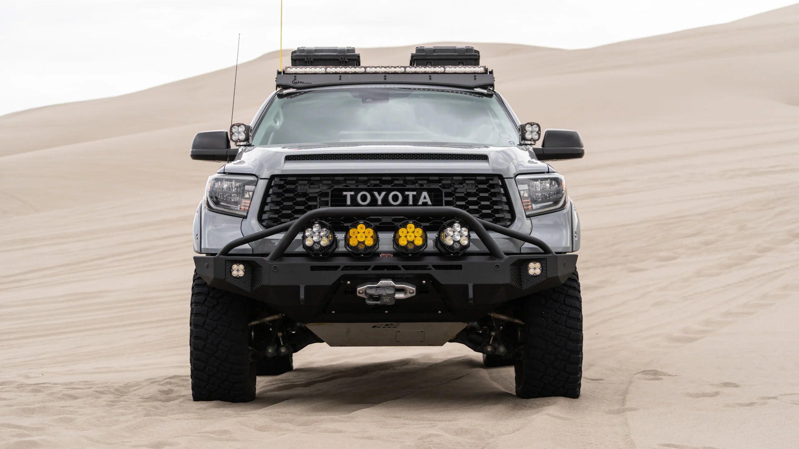 Modified Toyota Tundra with off-road lights and roof racks on desert sand dunes