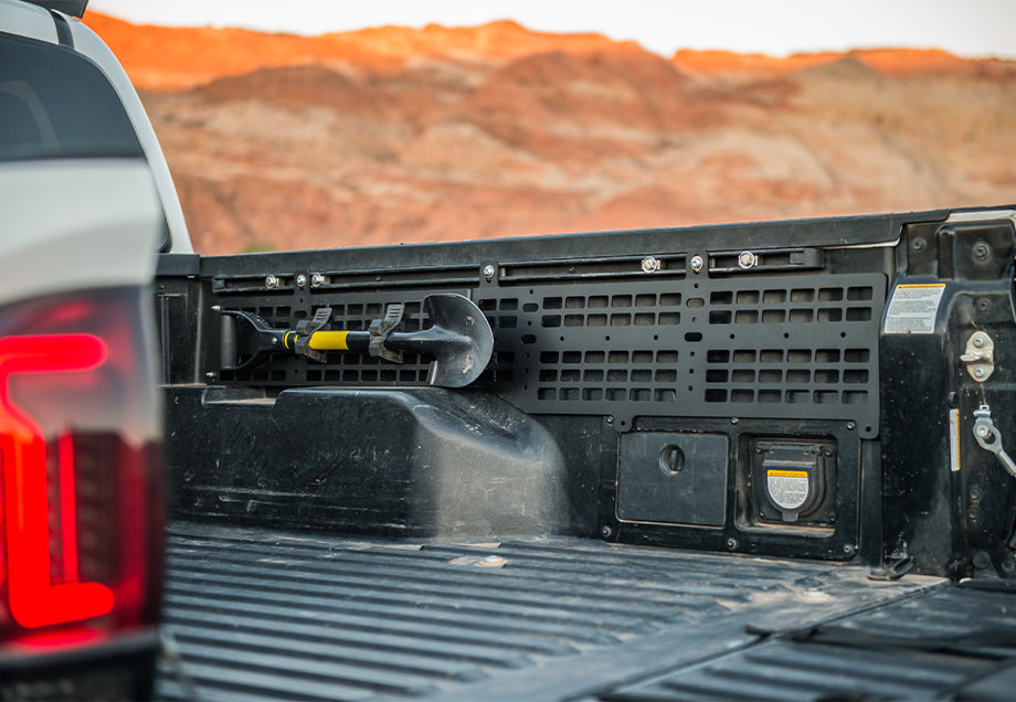 Toyota Tacoma truck bed with a black molle panel and mounted shovel in a desert landscape