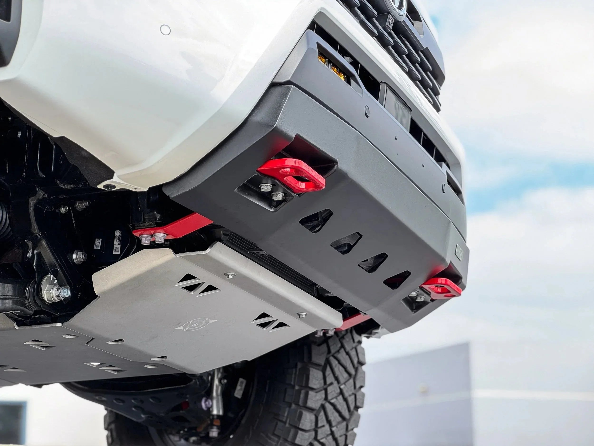 Aftermarket off-road front bumper and skid plate on Toyota truck with red tow hooks