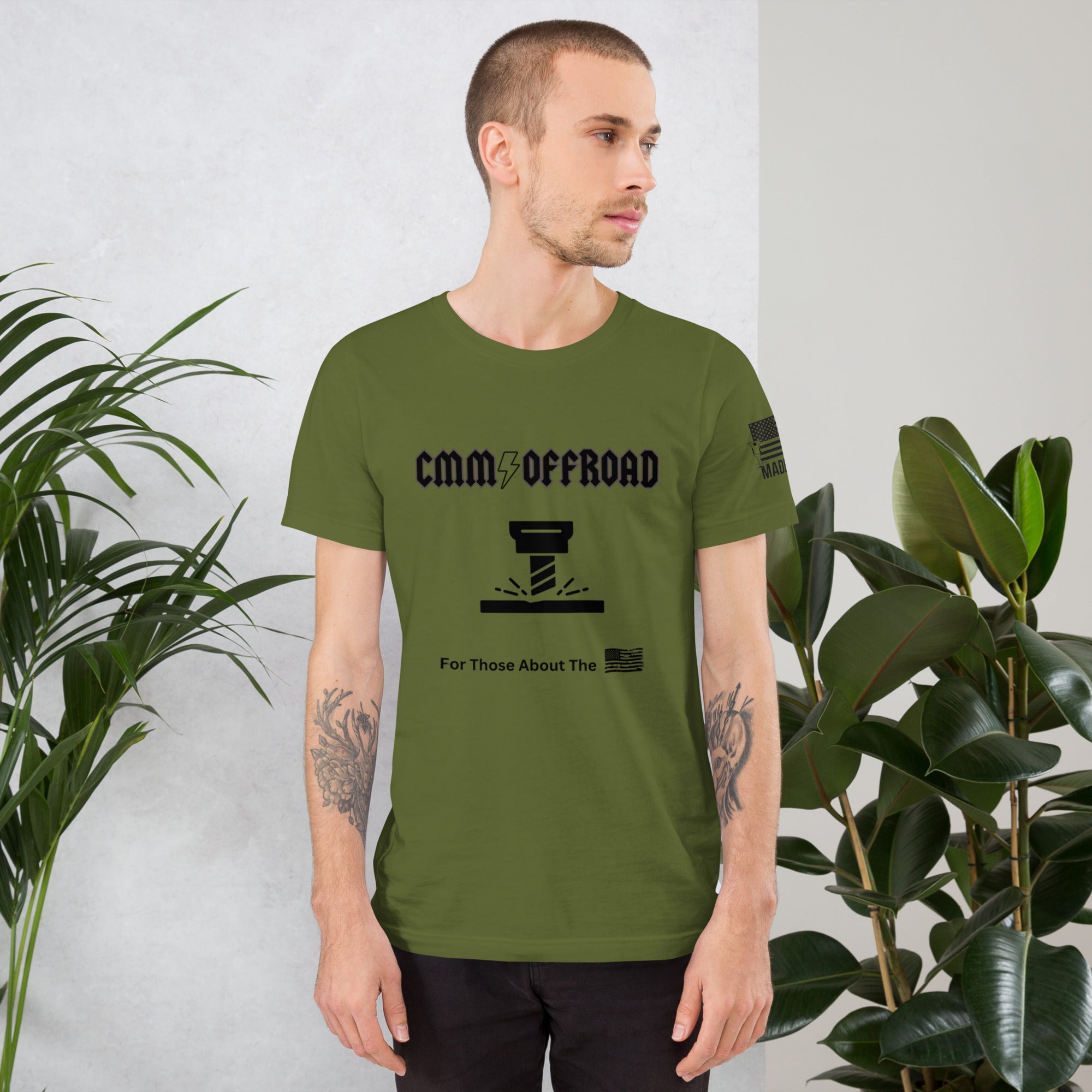 Man wearing olive green offroad graphic t-shirt, standing indoors by plants