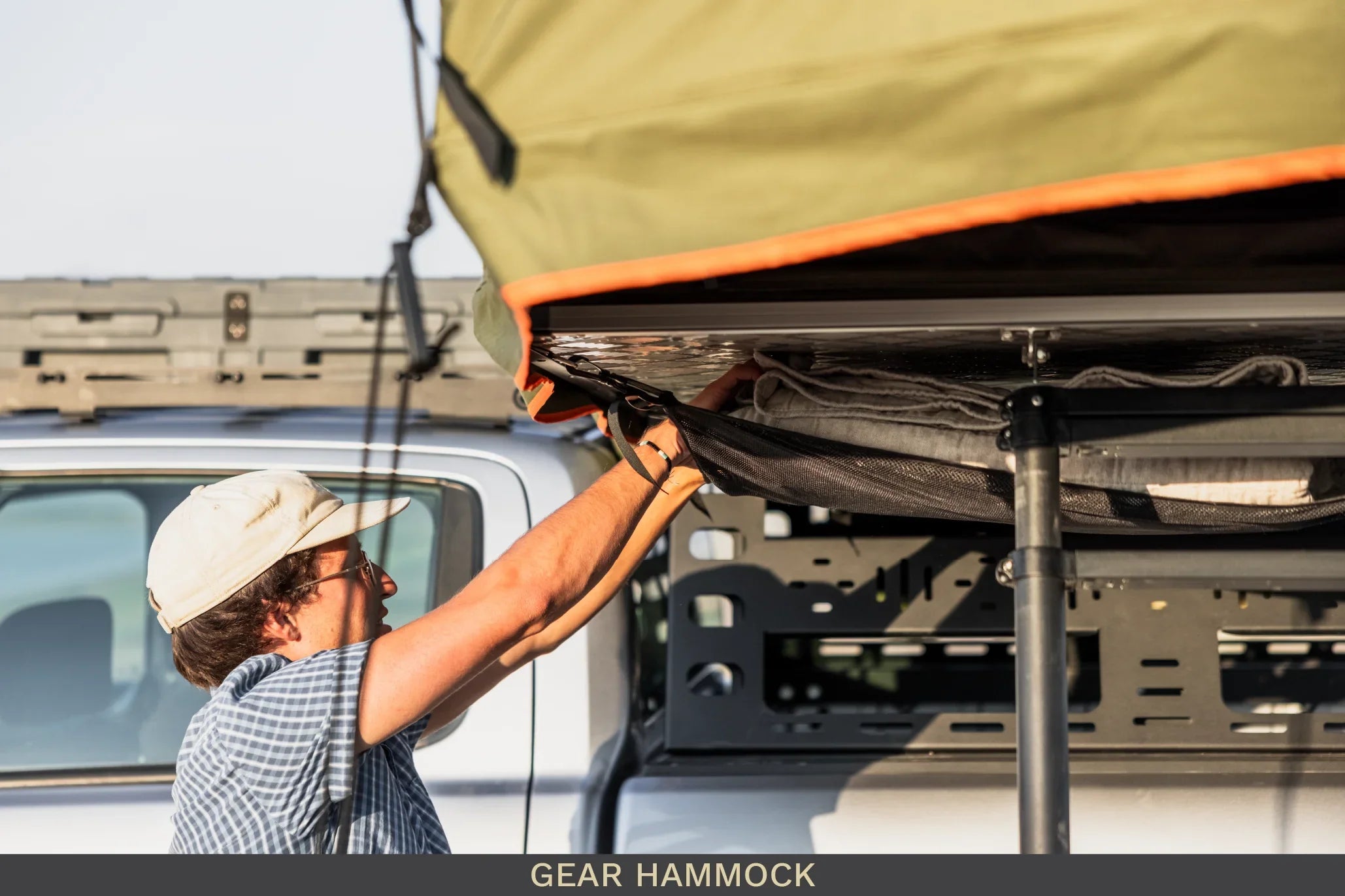 Person attaching overland camping gear hammock to vehicle rooftop tent rack outdoors