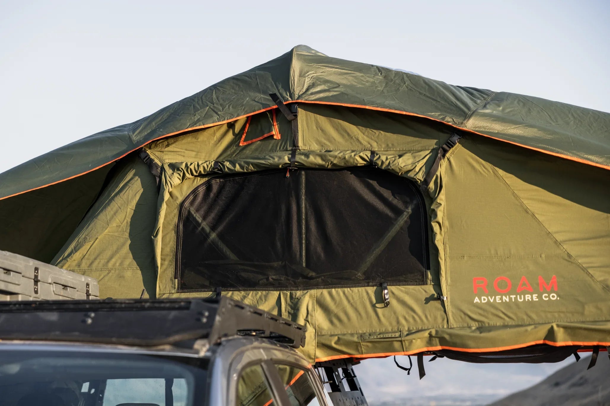 Green rooftop tent with mesh window for overlanding on vehicle, ROAM Adventure Co. logo visible
