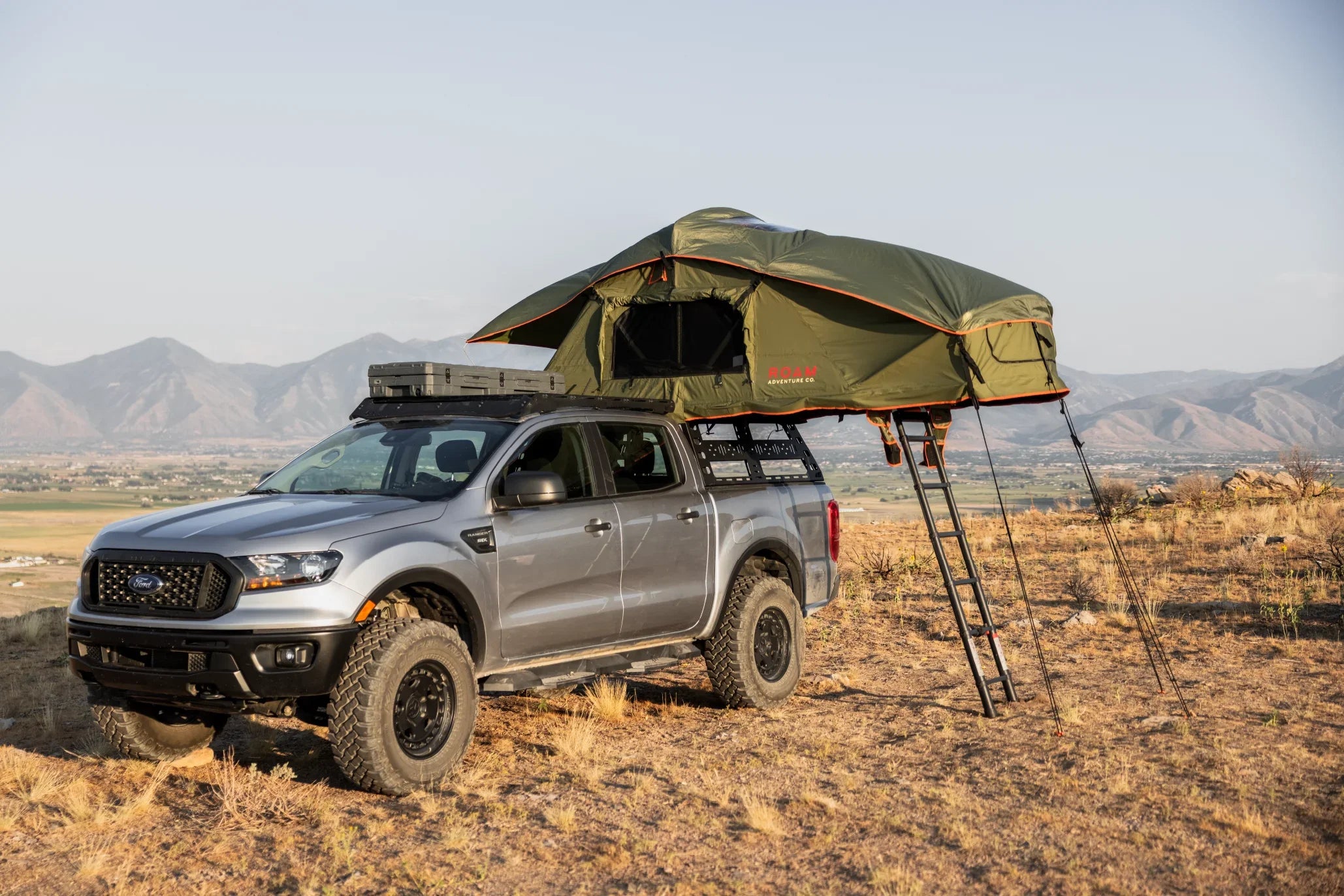 Ford truck with rooftop overland tent and gear, parked on a scenic mountain hillside