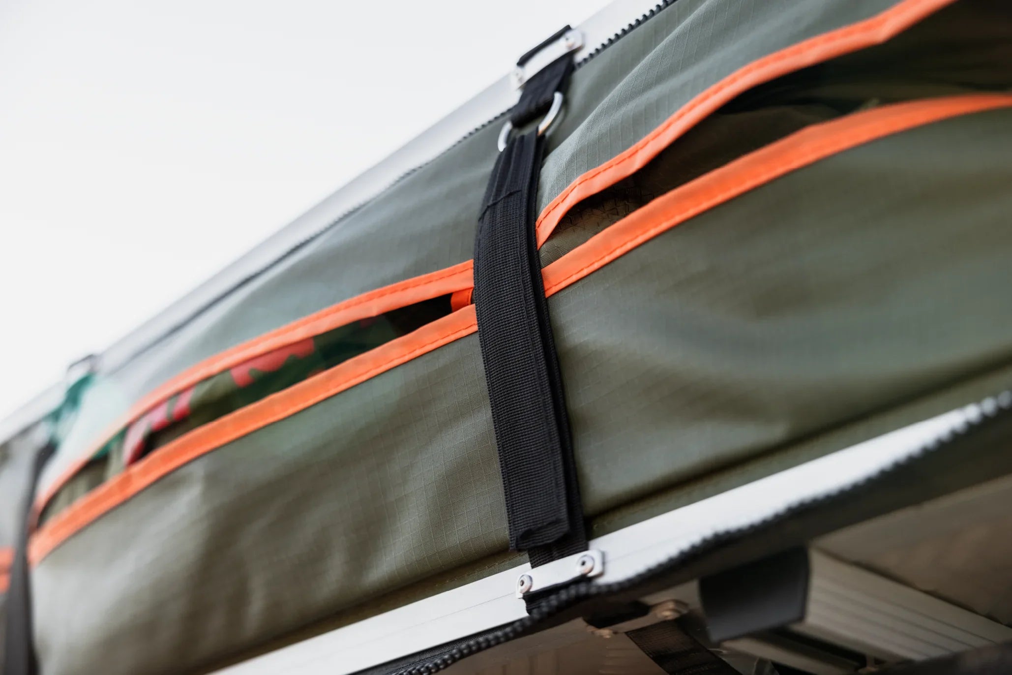 Close-up of rugged green camping gear storage bag with orange zippers and black strap, ideal for overlanding