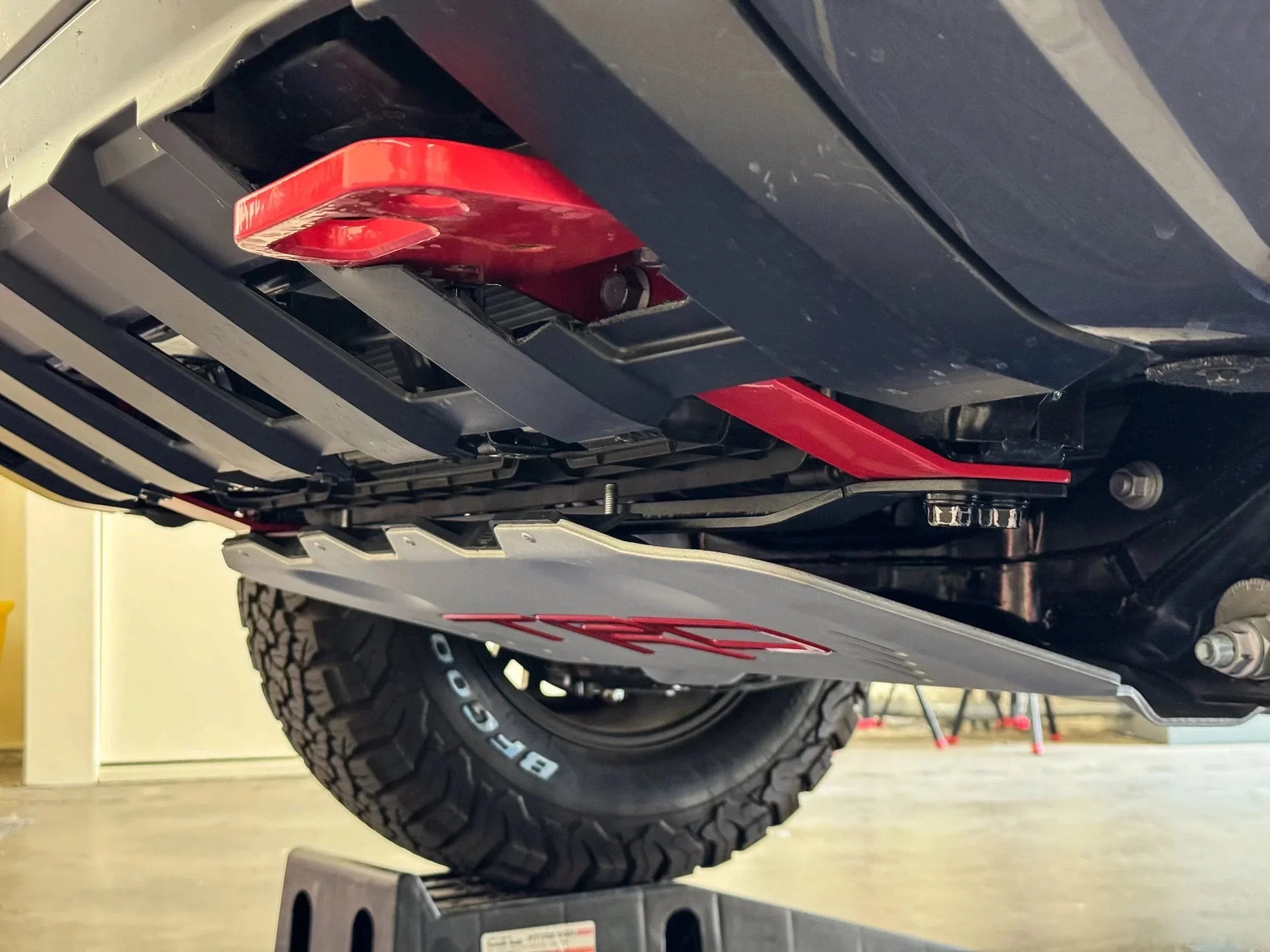 Off-road vehicle skid plate and red recovery point under chassis, all-terrain BG Goodrich tire visible.