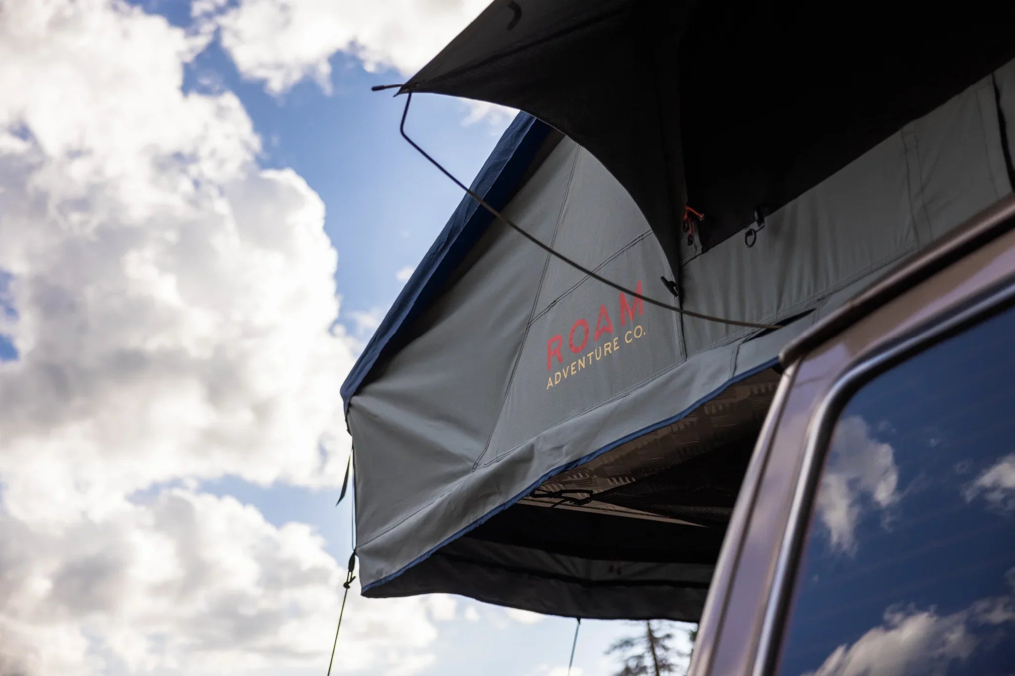 Vehicle rooftop tent for overlanding and camping with Roam Adventure Co. logo, outdoor sky background