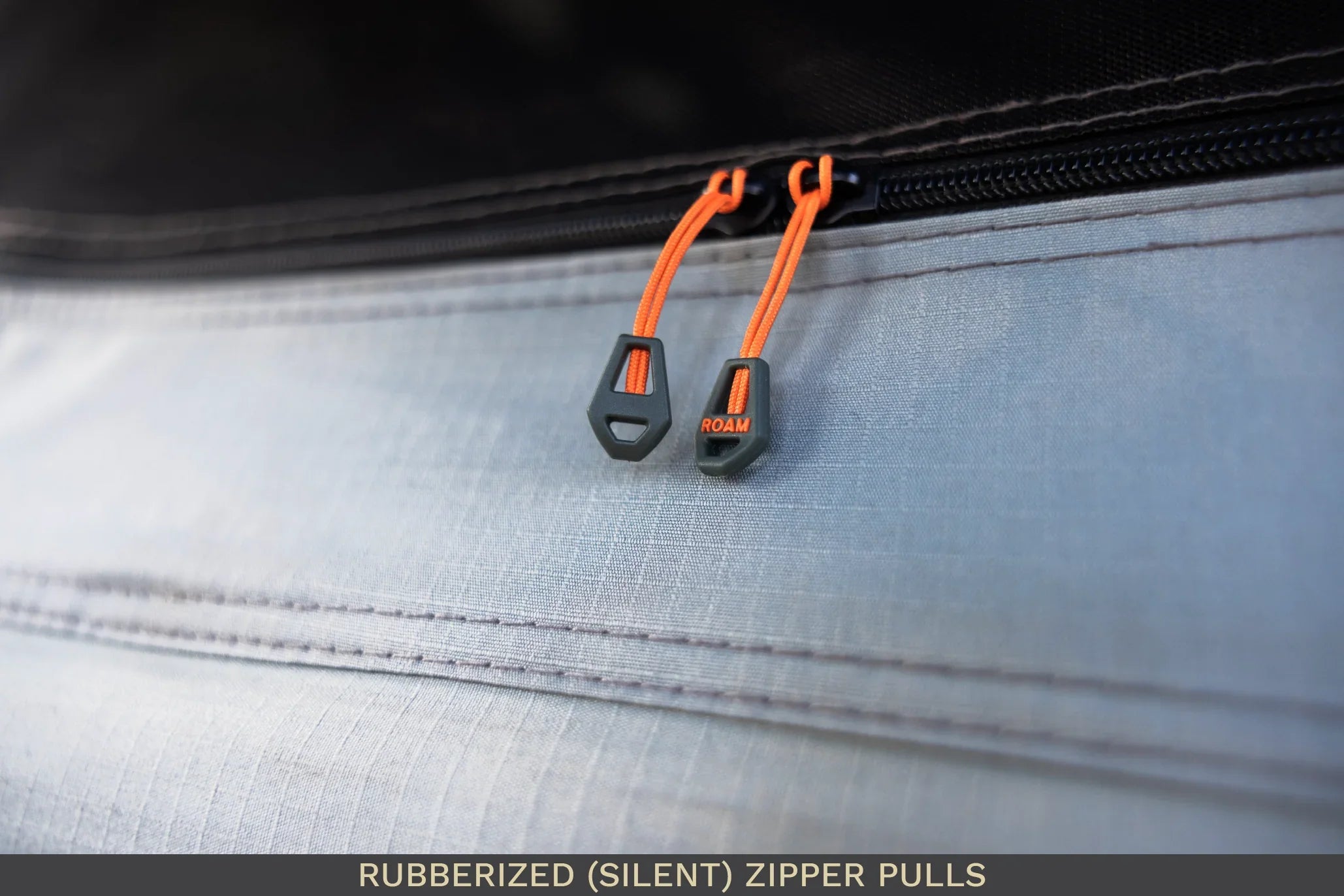 Close-up of rubberized silent zipper pulls with orange cords on outdoor gear fabric