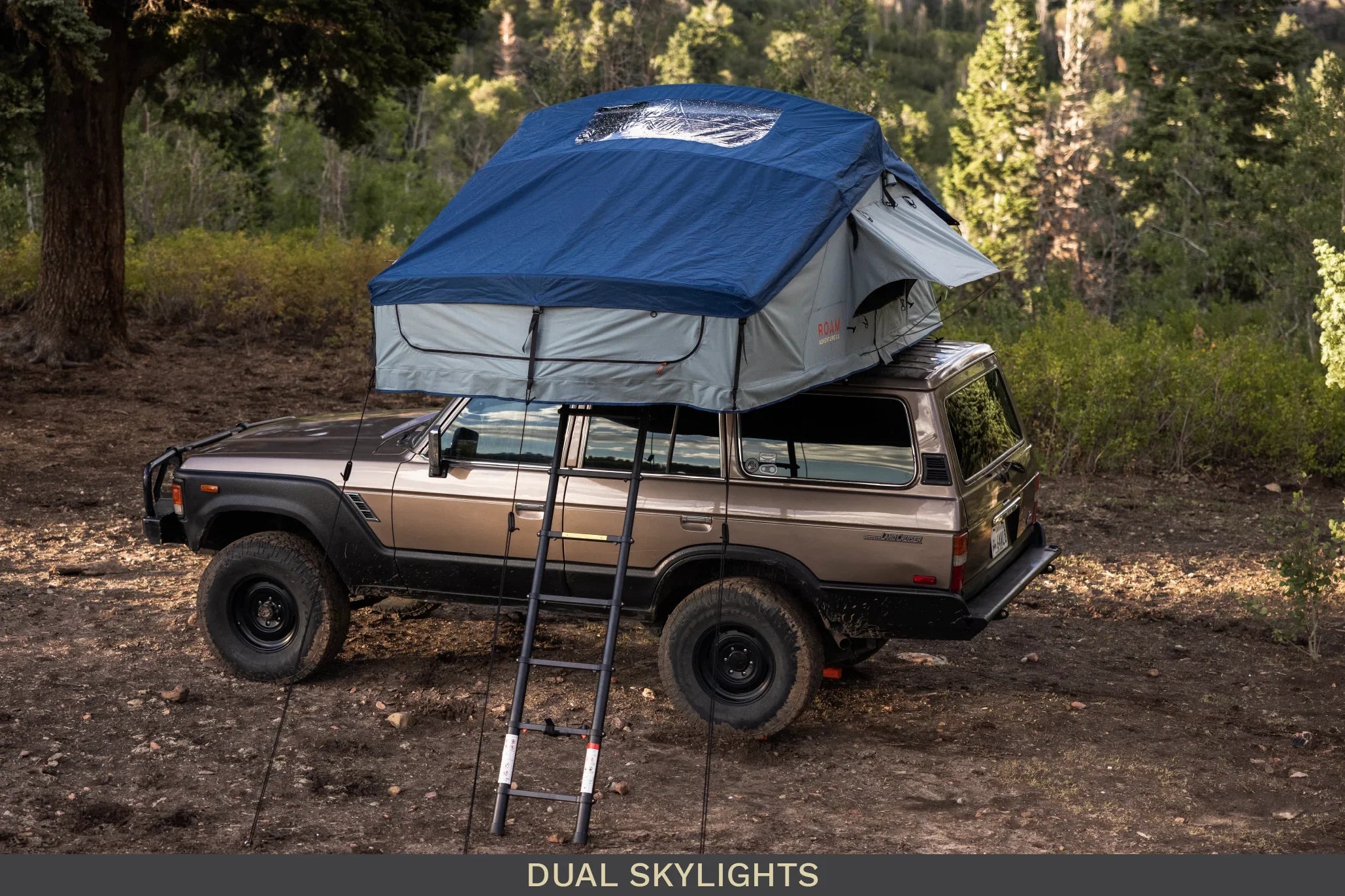 SUV with rooftop tent and ladder set up for overlanding in a forest campsite
