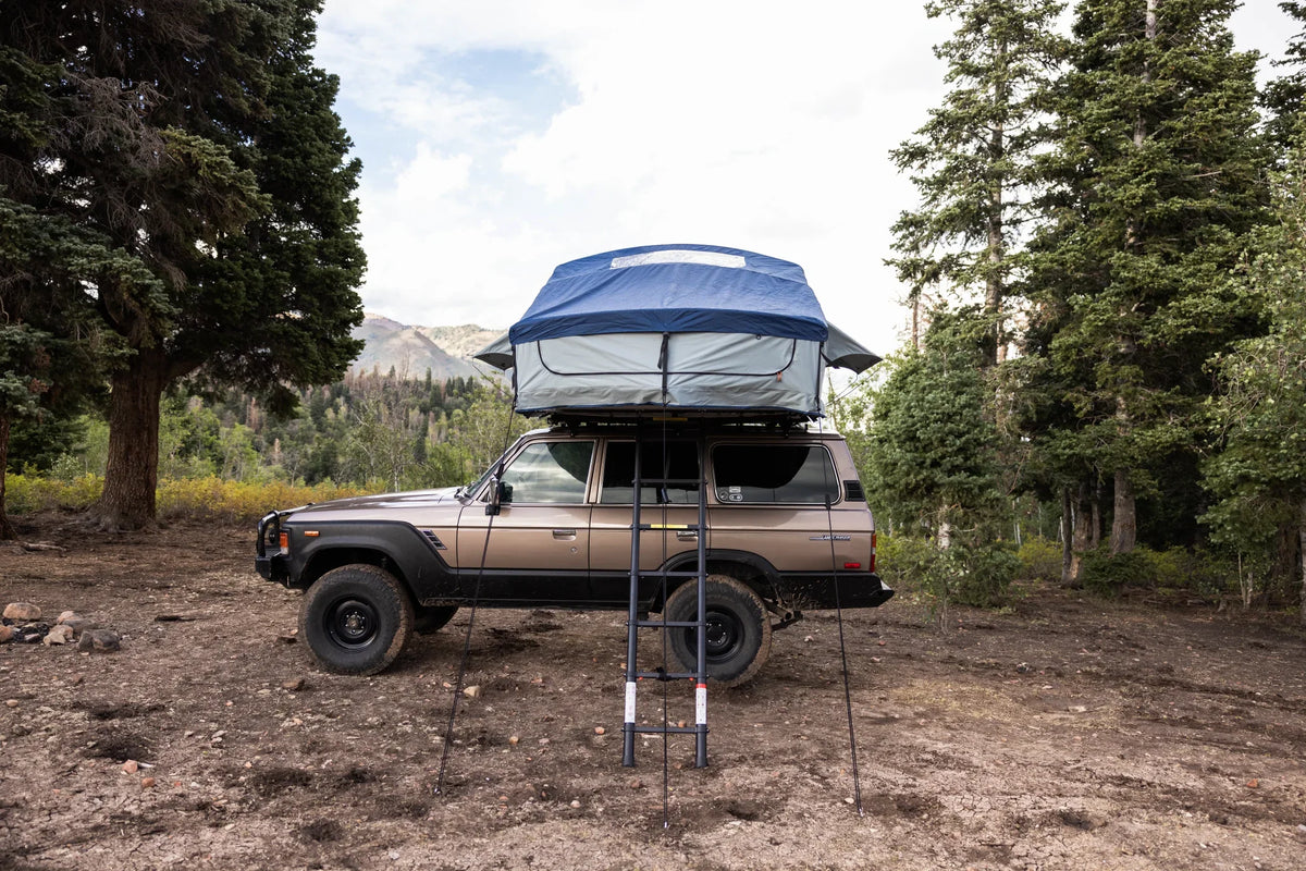 SUV with a rooftop tent set up for overlanding in a forested camping area