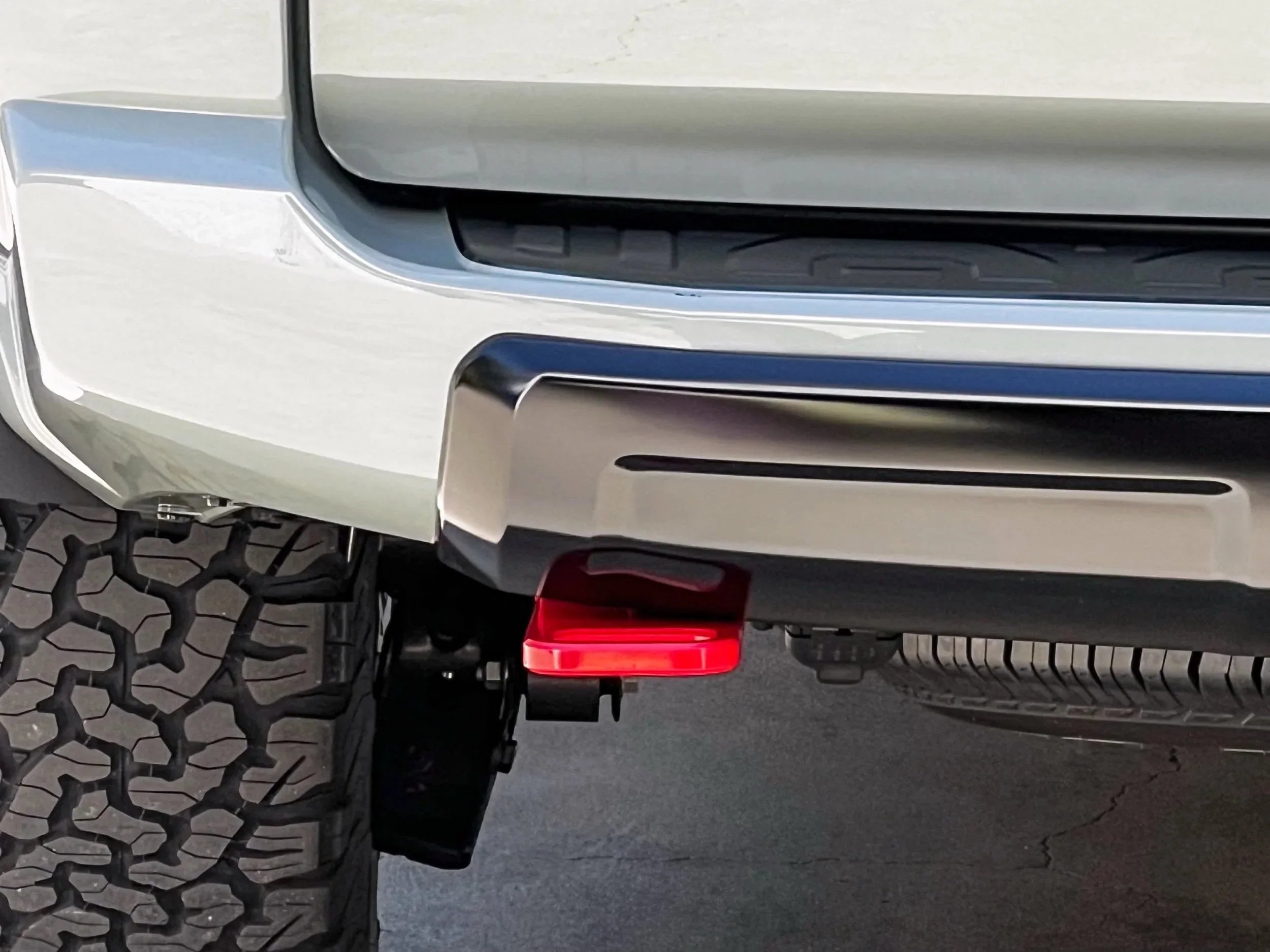Close-up of off-road vehicle rear bumper, tire tread, and red tow hook attachment