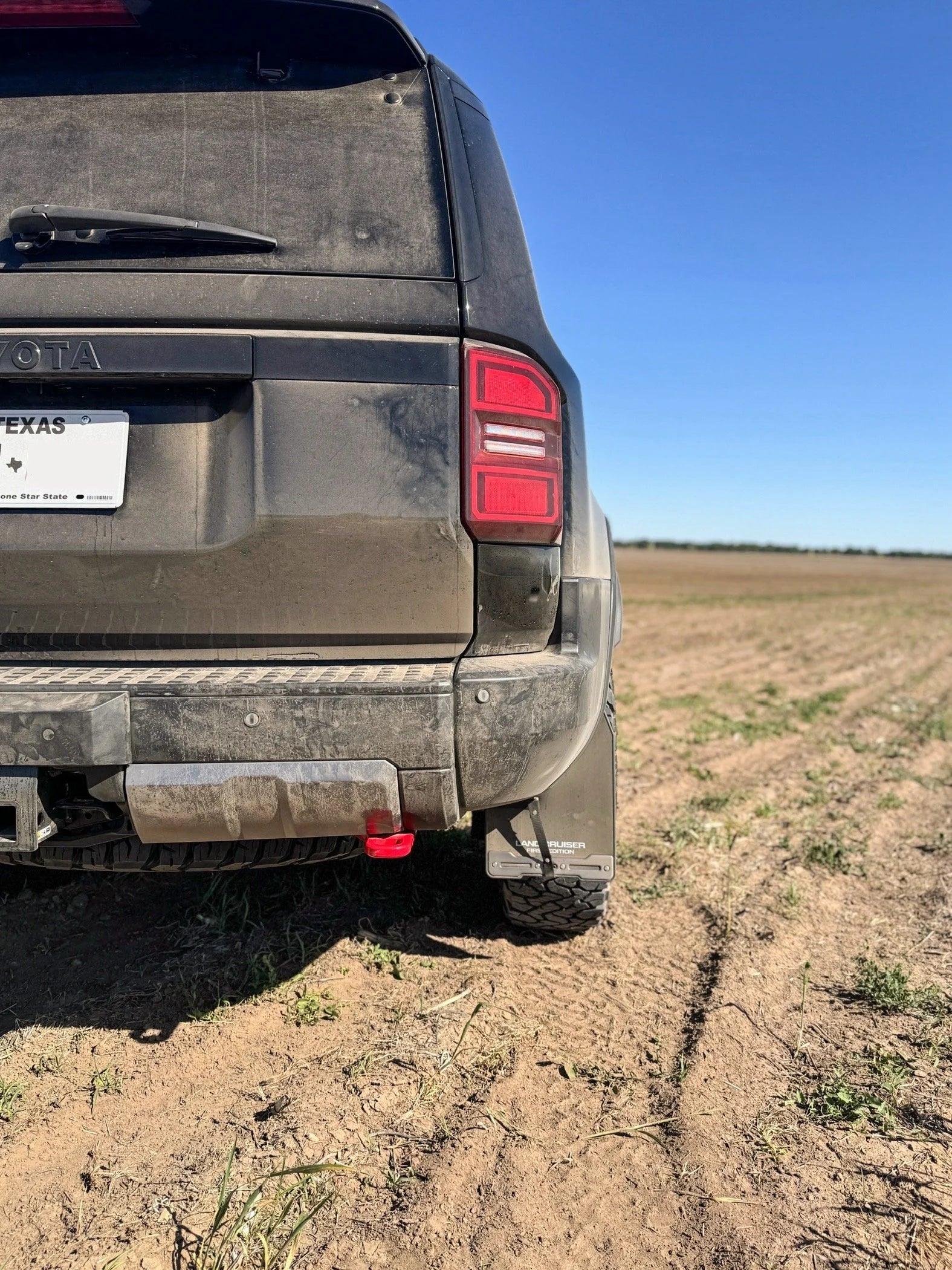 Dirty Toyota SUV rear view with mud flaps on a dirt trail under a clear blue sky