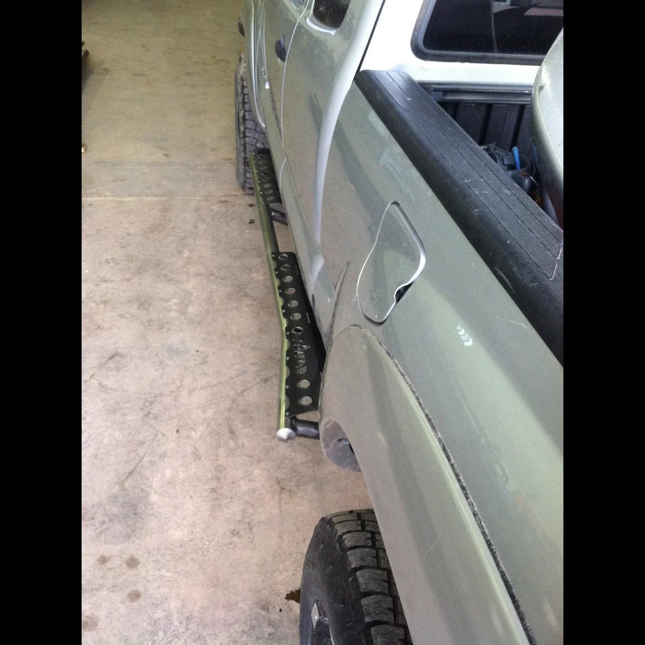 Toyota Tacoma side view with black off-road rock sliders installed in a garage