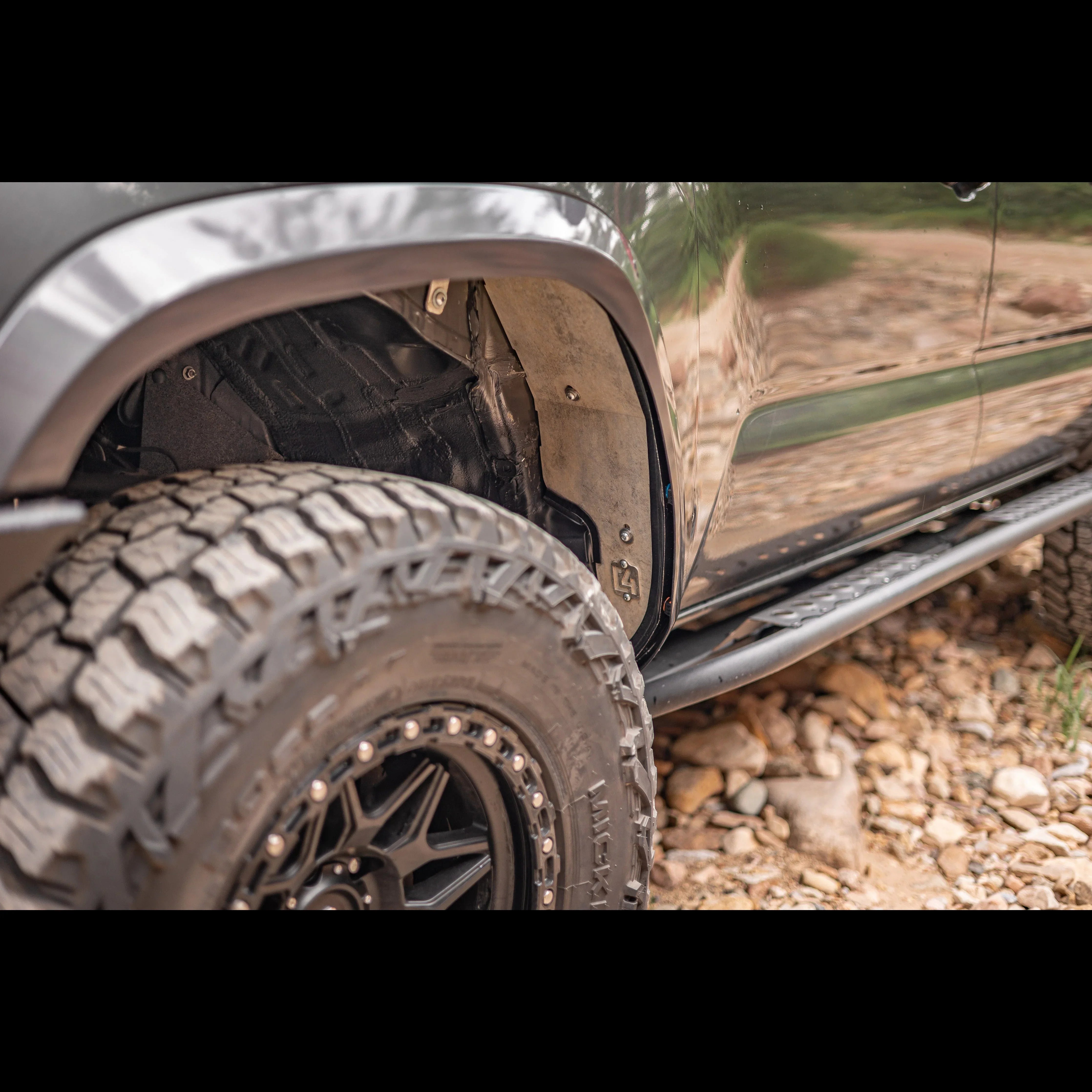 Close-up of off-road truck tire, wheel well, rock sliders, and rugged terrain