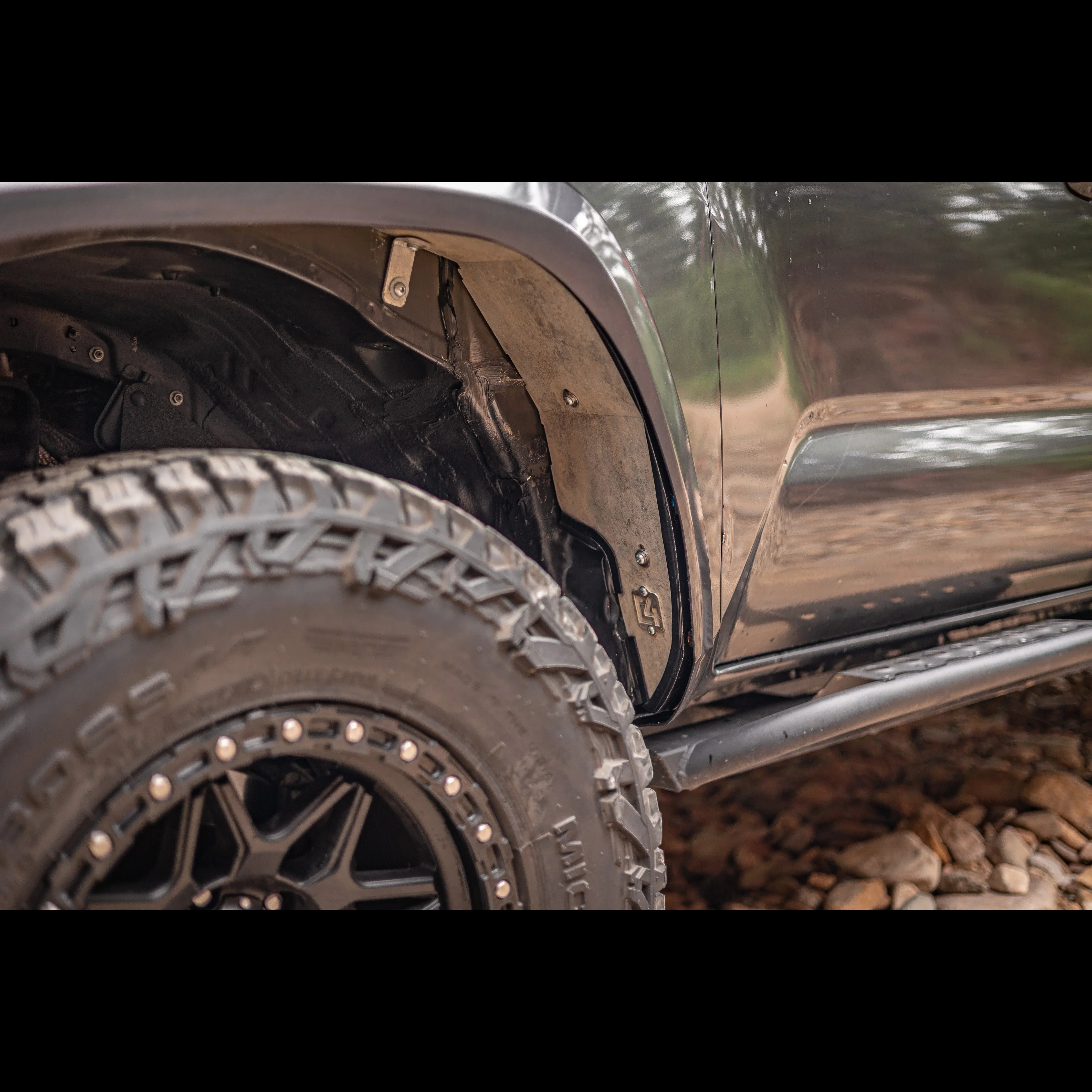 Close-up of off-road truck with rugged fender liner, all-terrain tire, and rock slider