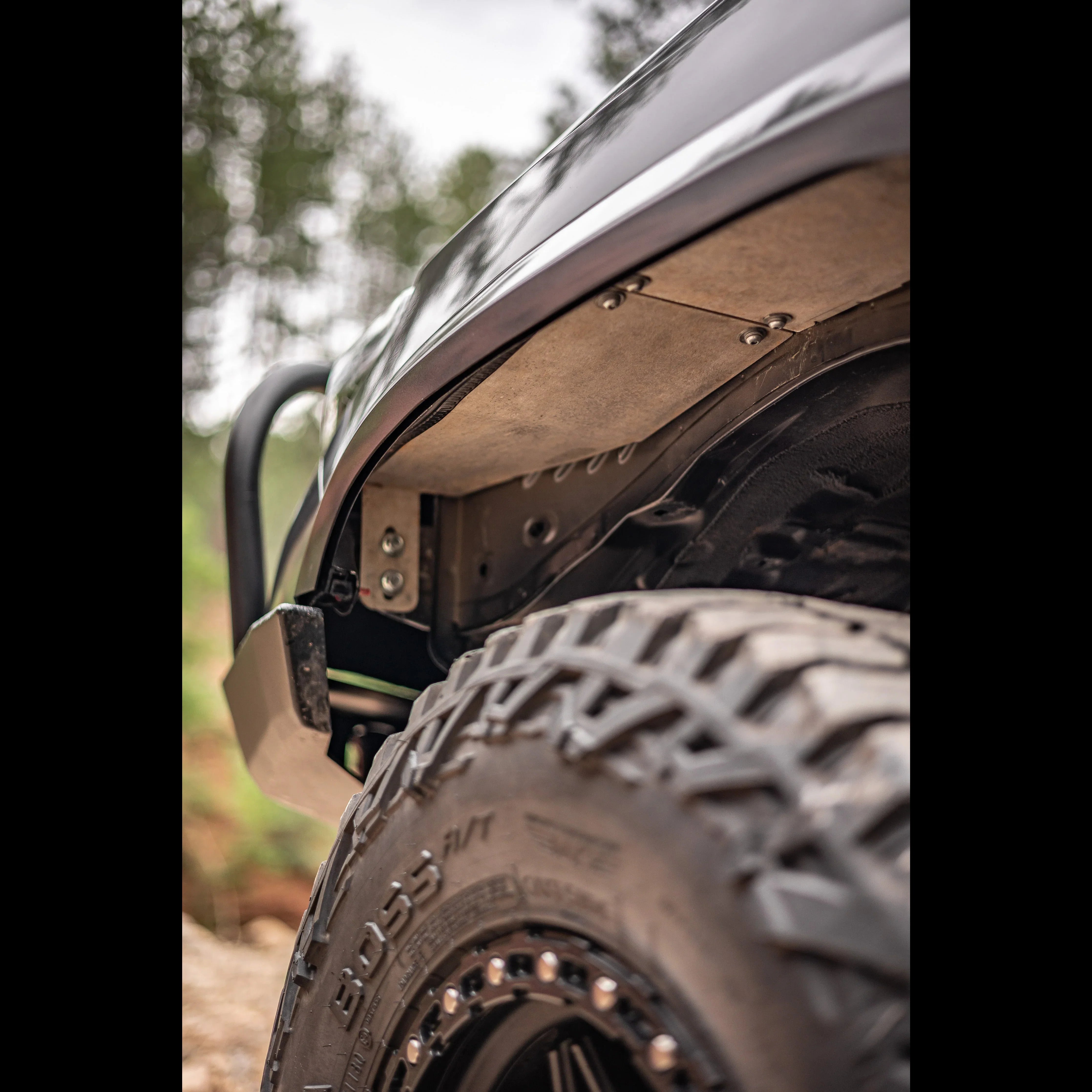 Close-up of off-road vehicle fender liner and rugged all-terrain tire in forest setting