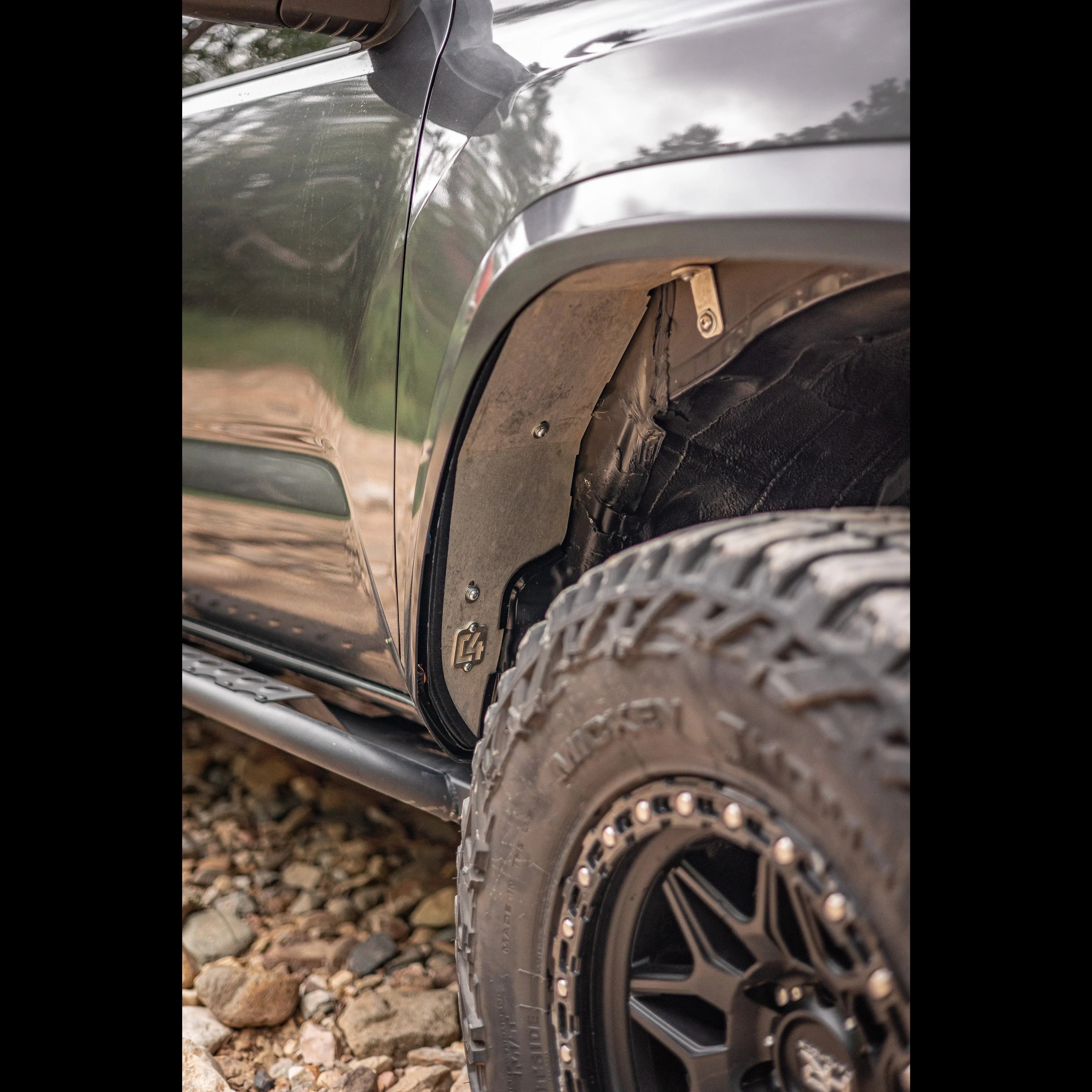 Close-up of off-road vehicle fender liner, all-terrain tire, and rock slider on rocky trail