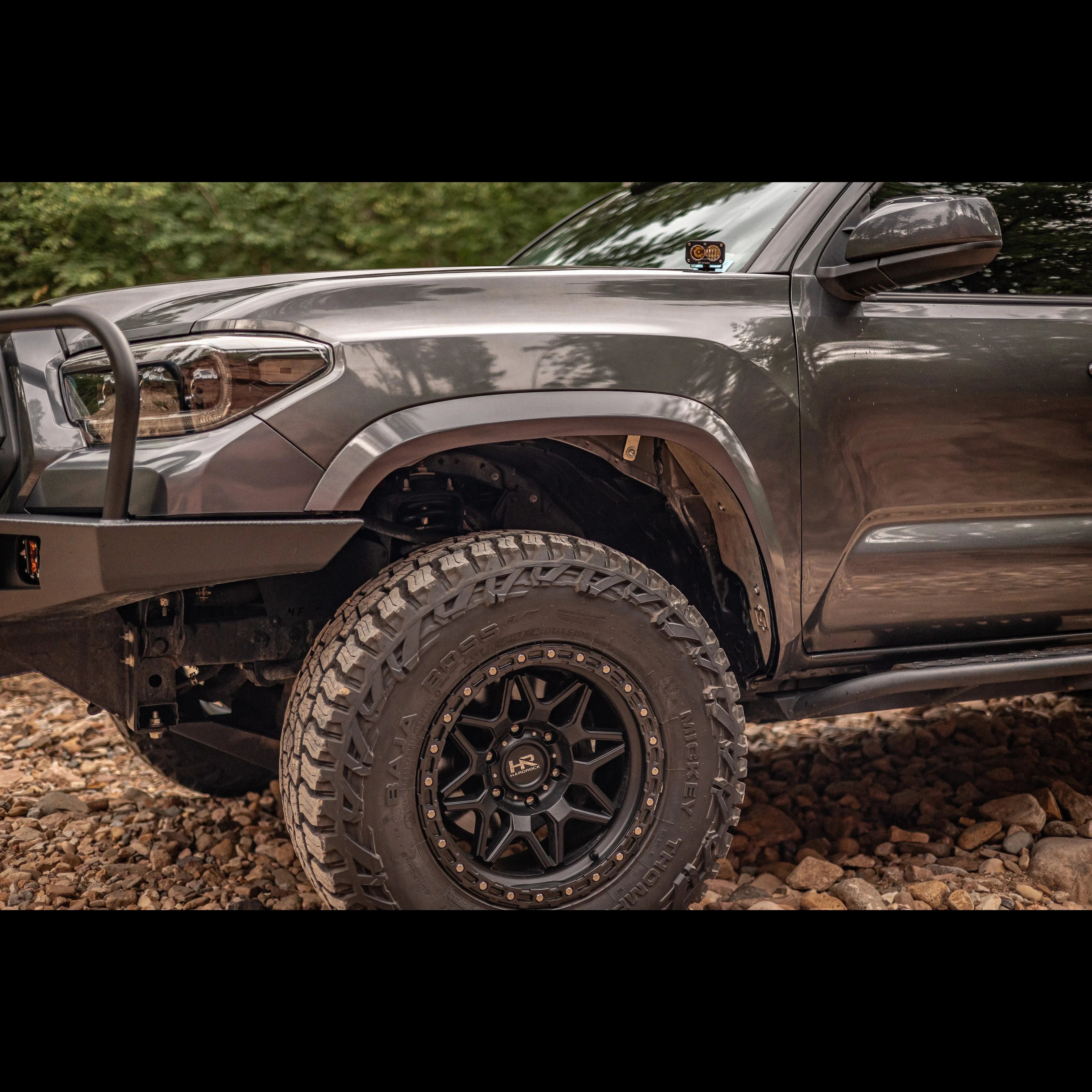 Toyota Tacoma with off-road wheels, tires, and rock sliders on a rocky trail