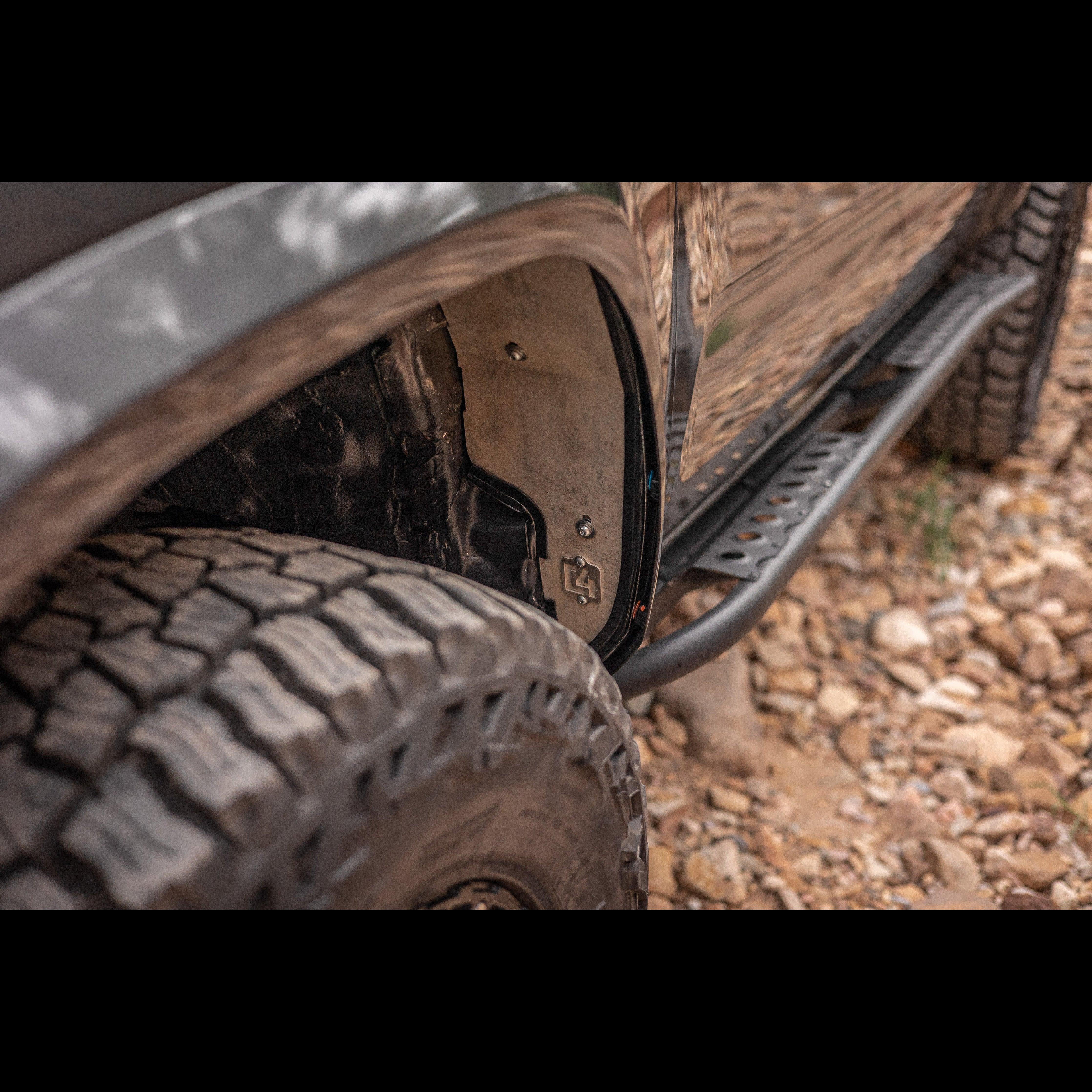 Close-up of off-road vehicle fender liner, rock slider, and all-terrain tire on rocky trail