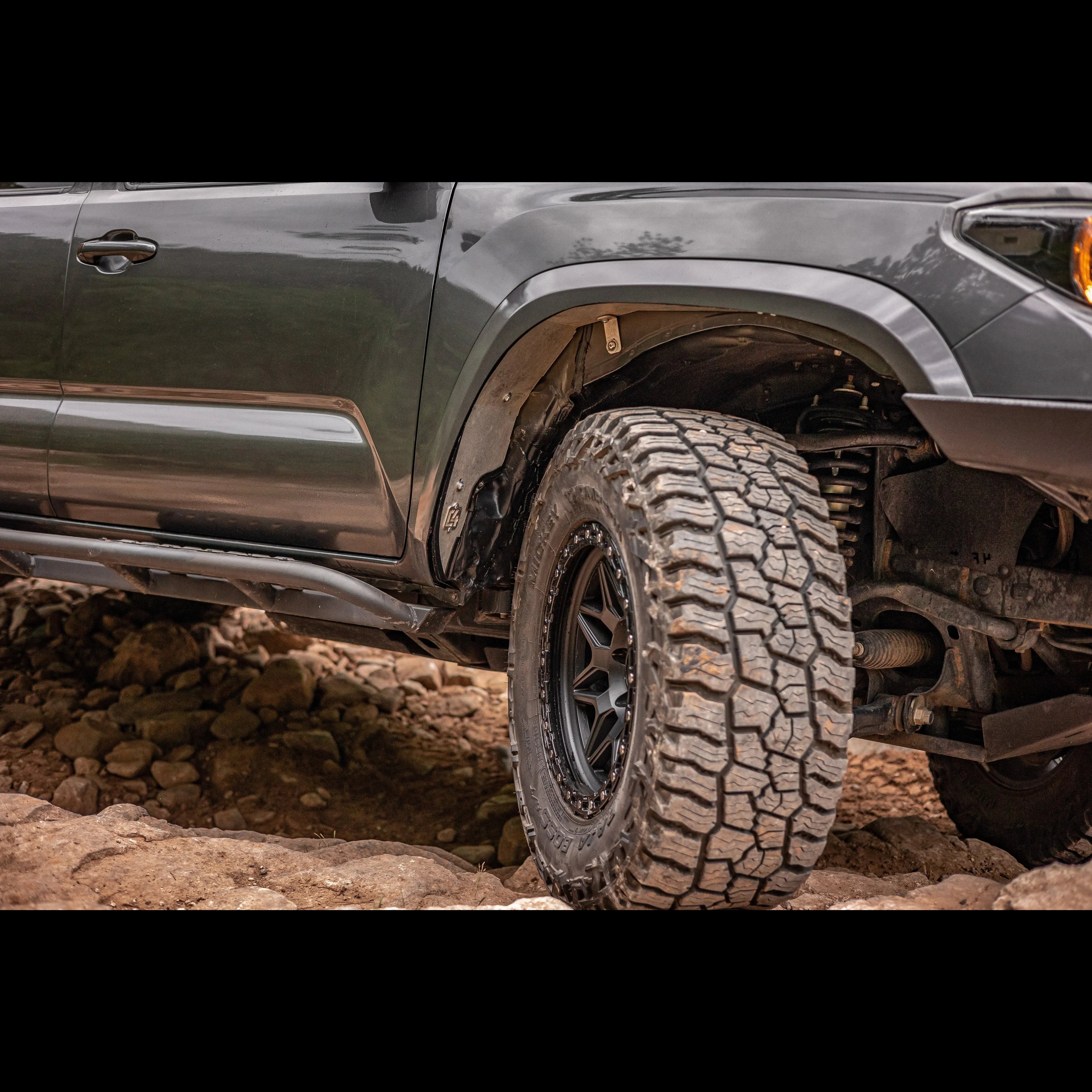 Toyota Tacoma off-road with all-terrain tires and rock sliders on rocky trail