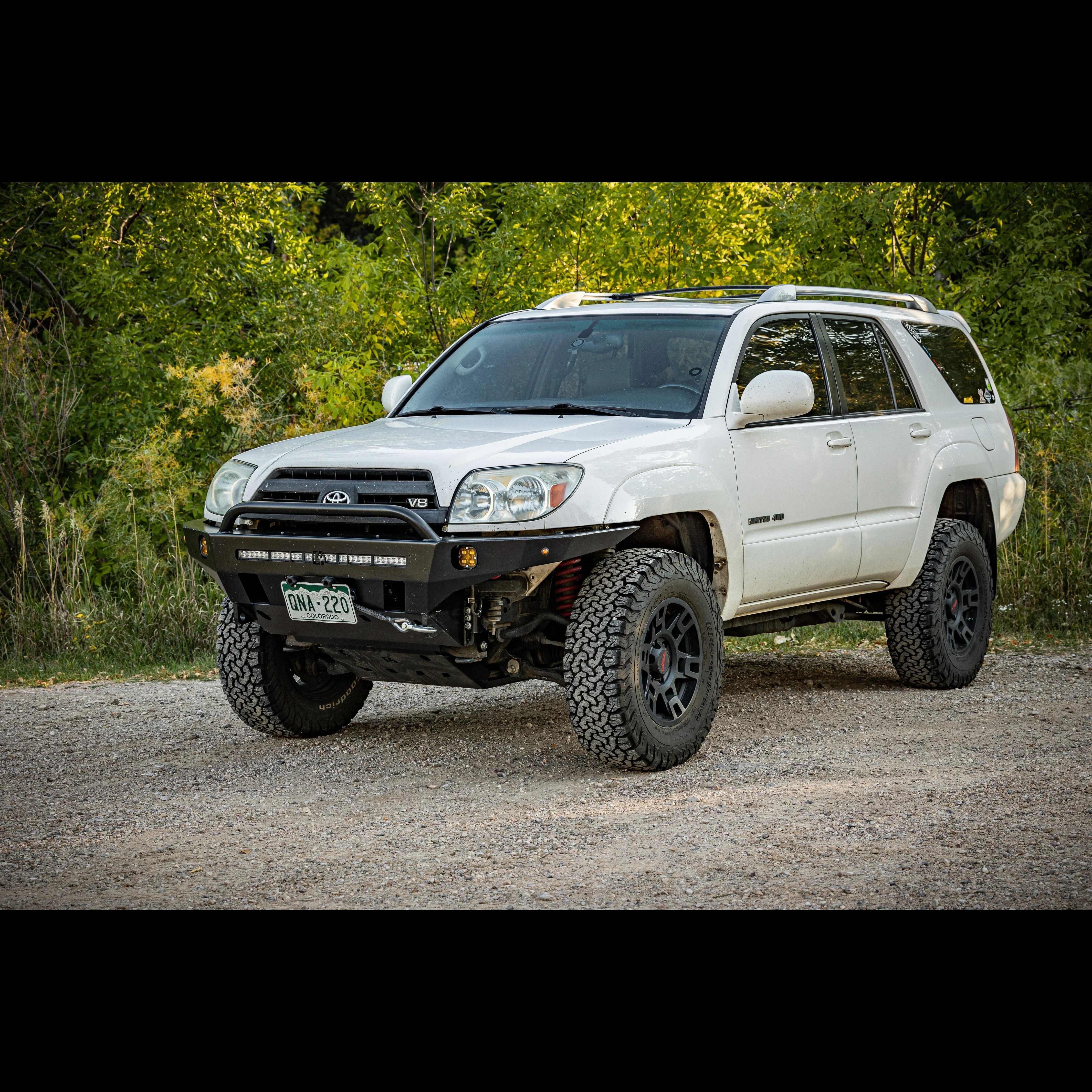 White Toyota 4Runner SUV with off-road tires and aftermarket front bumper on gravel path
