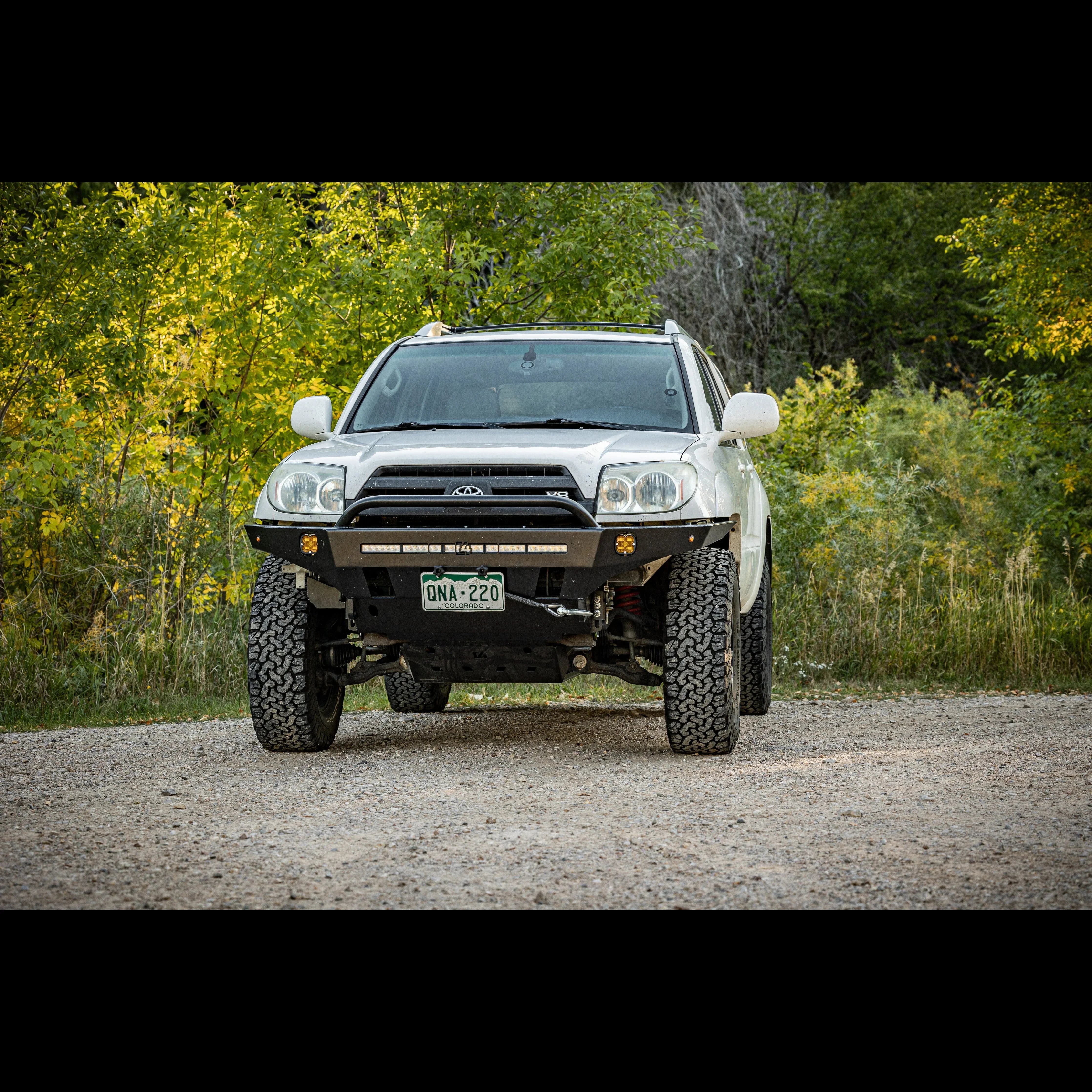 Lifted Toyota 4Runner with off-road front bumper on a gravel trail surrounded by trees
