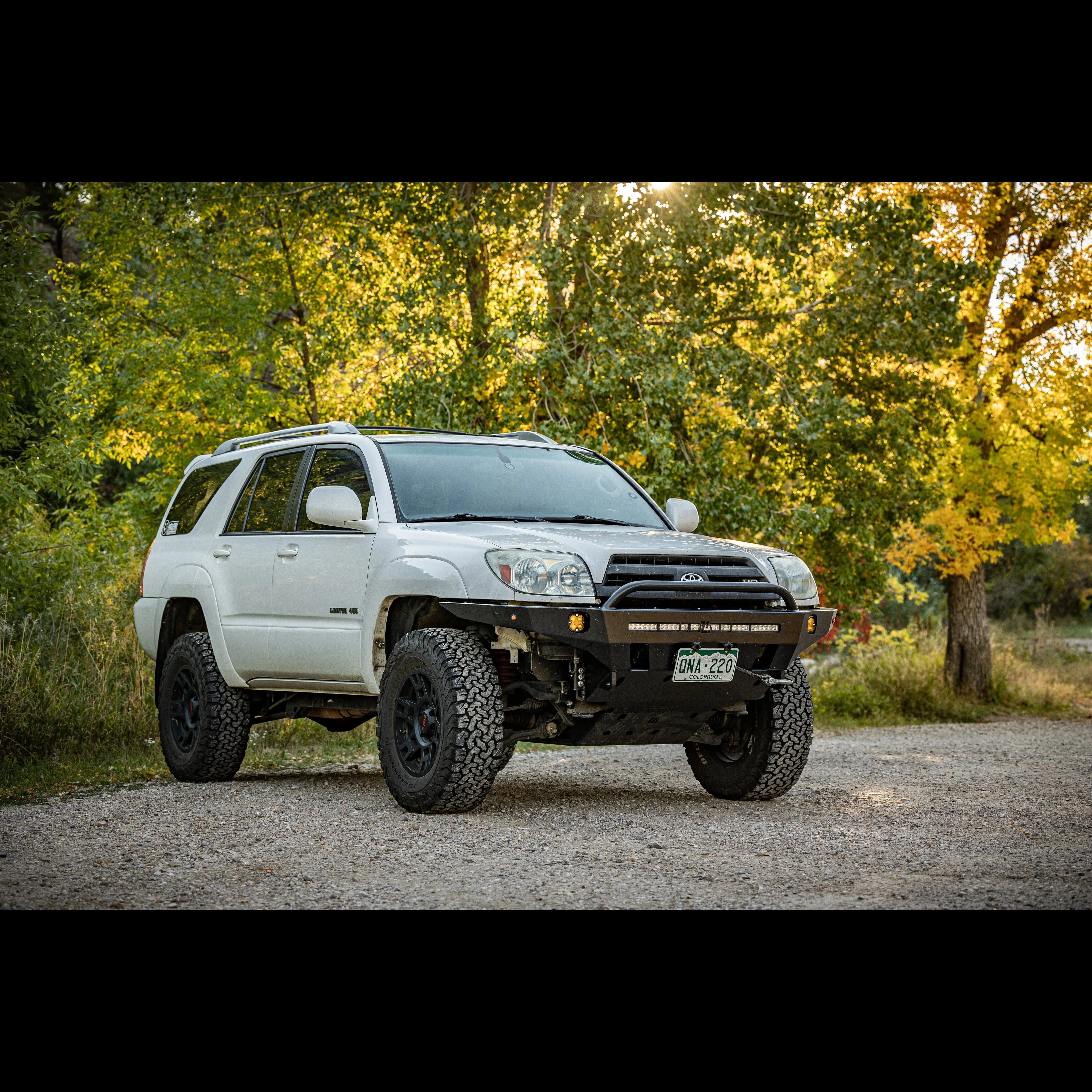 White Toyota 4Runner SUV with off-road tires and steel bumper parked outdoors in nature