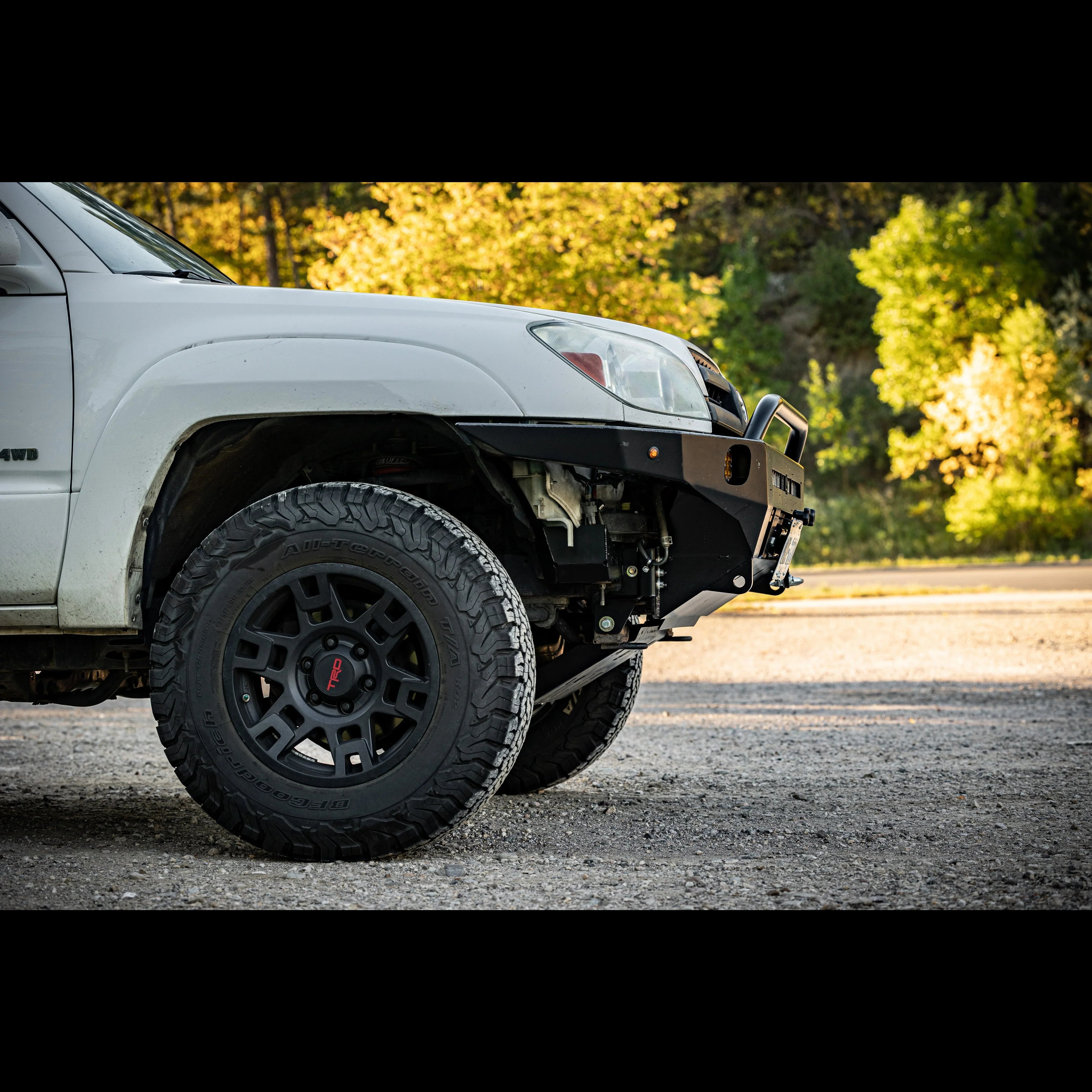 Off-road Toyota Tacoma with aftermarket front bumper and all-terrain tires in sunlight