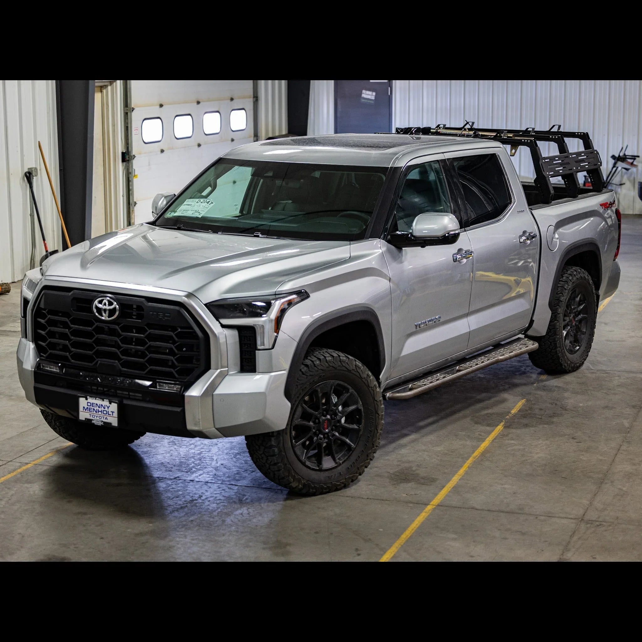 Silver Toyota Tundra with off-road tires and overland bed rack inside a garage
