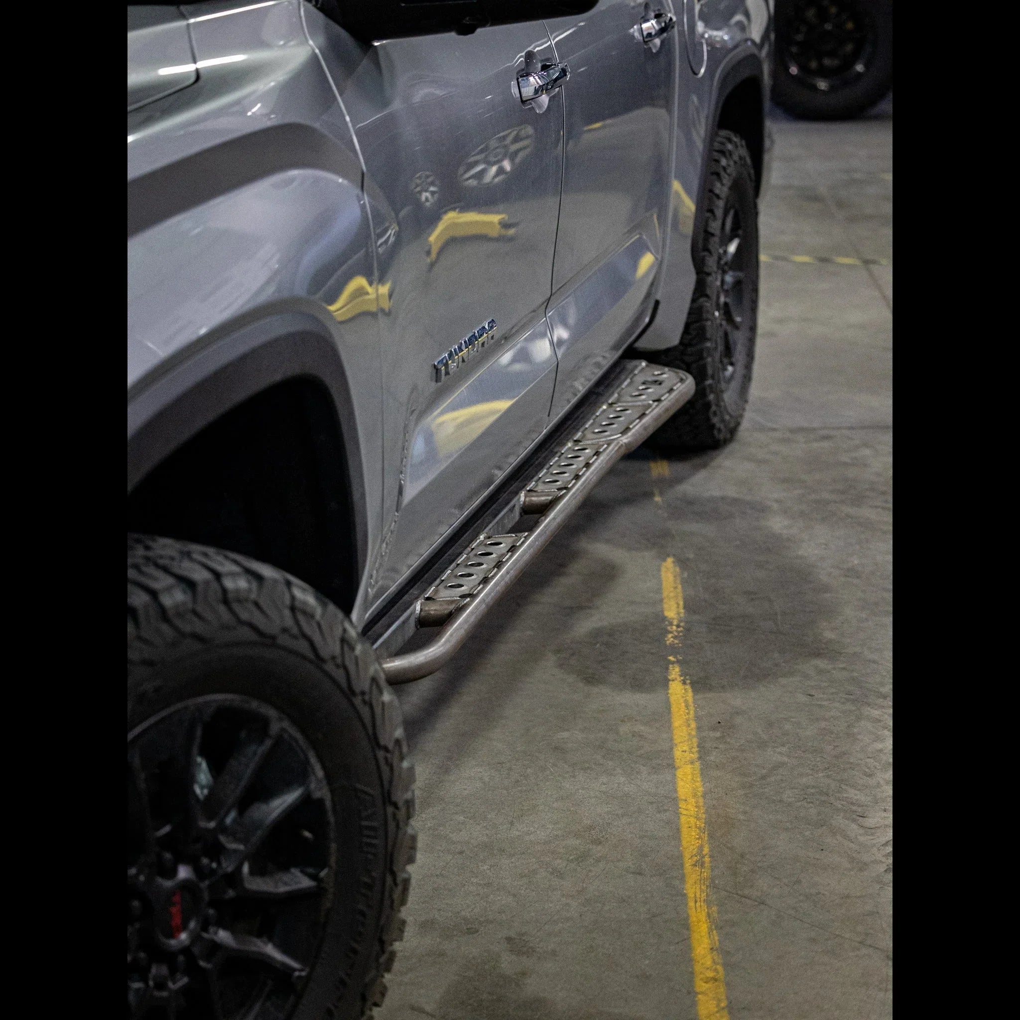 Toyota Tacoma with rugged off-road rock sliders and black alloy wheels in a garage