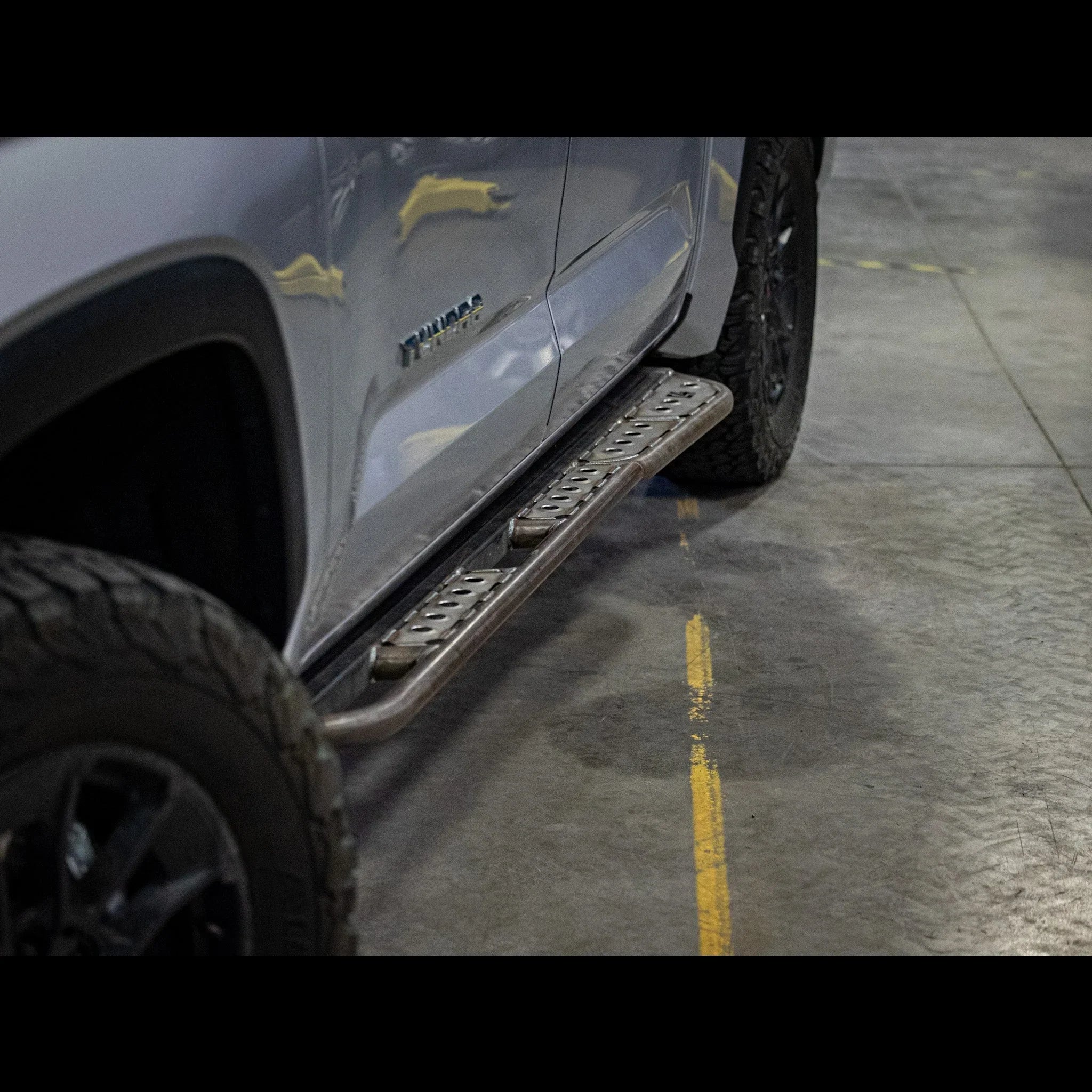 Toyota Tundra with rugged steel side steps, off-road tires, in a garage setting