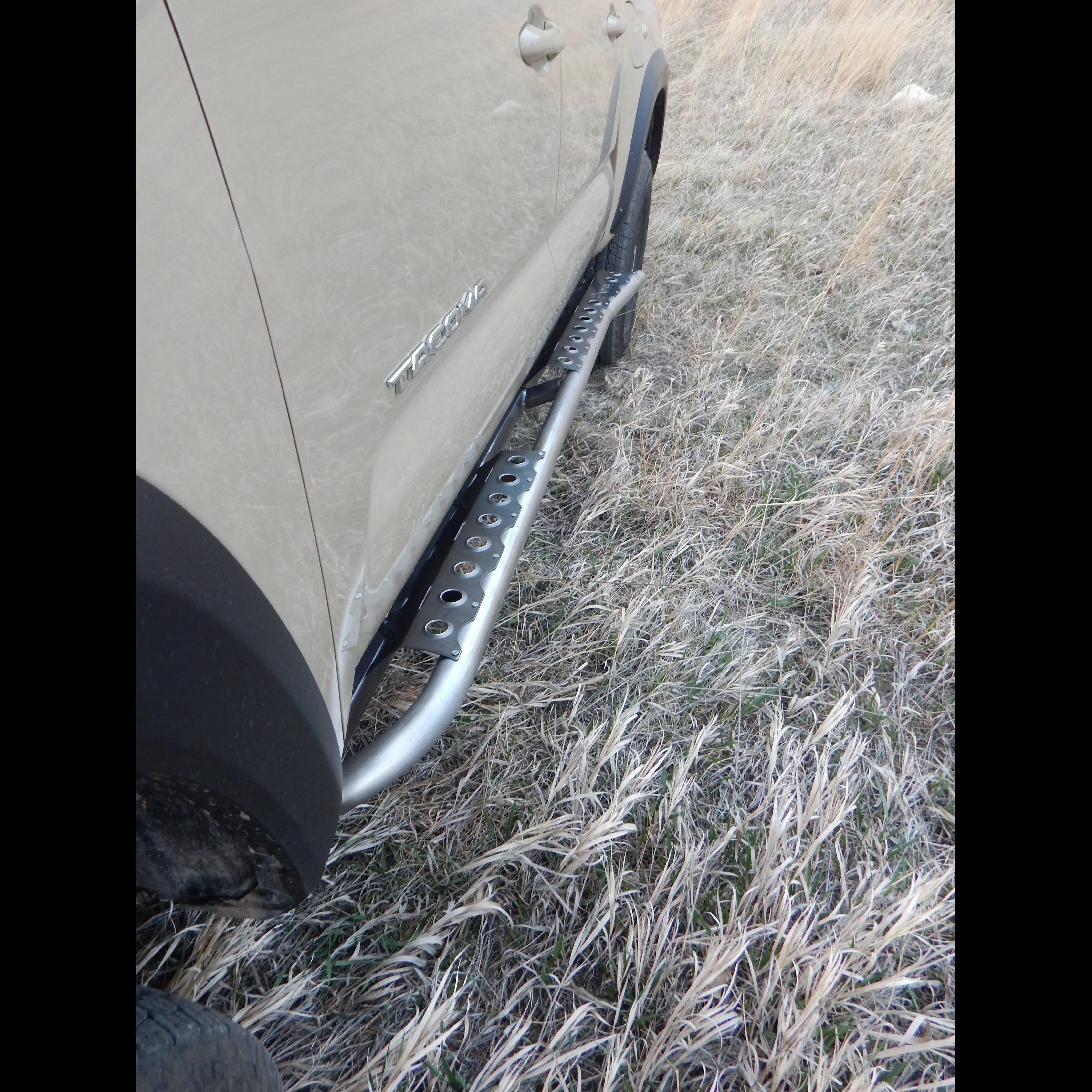 2016 Toyota Tacoma with steel rock slider step bar on grassy off-road terrain
