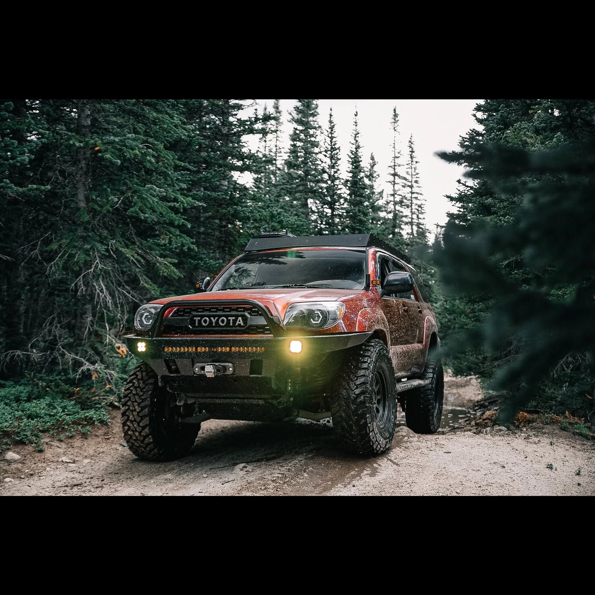 Lifted Toyota 4Runner with off-road tires and lights on a forest trail, overlanding ready.