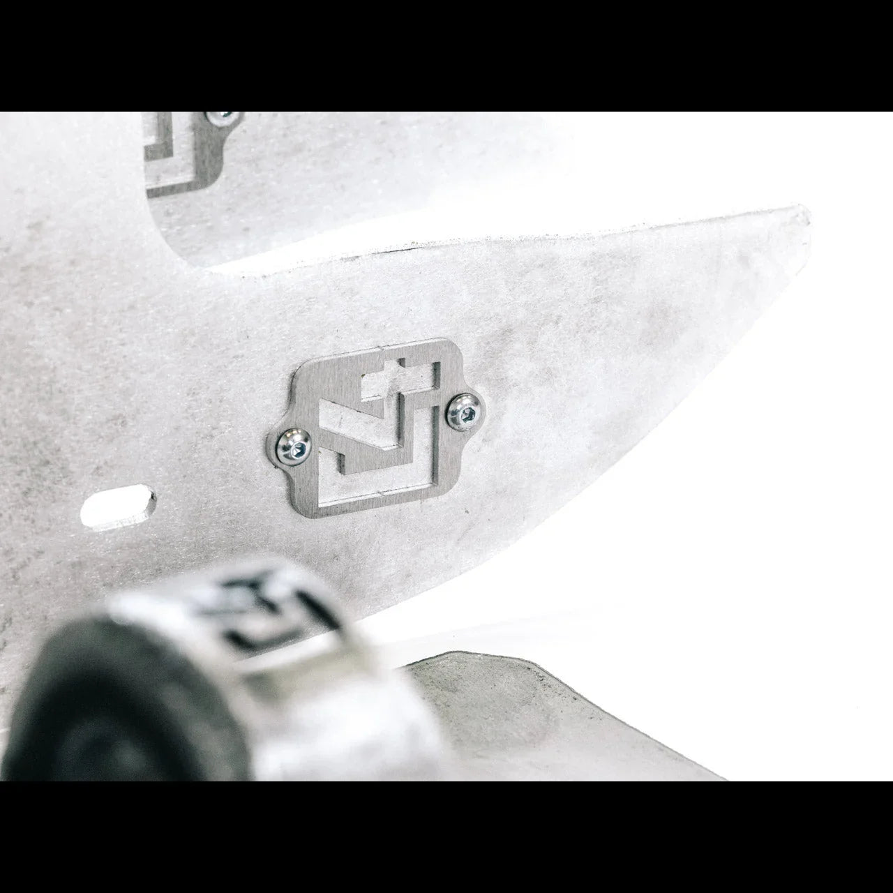 Close-up of an aluminum skid plate for off-road vehicles with cutout logo and screws.