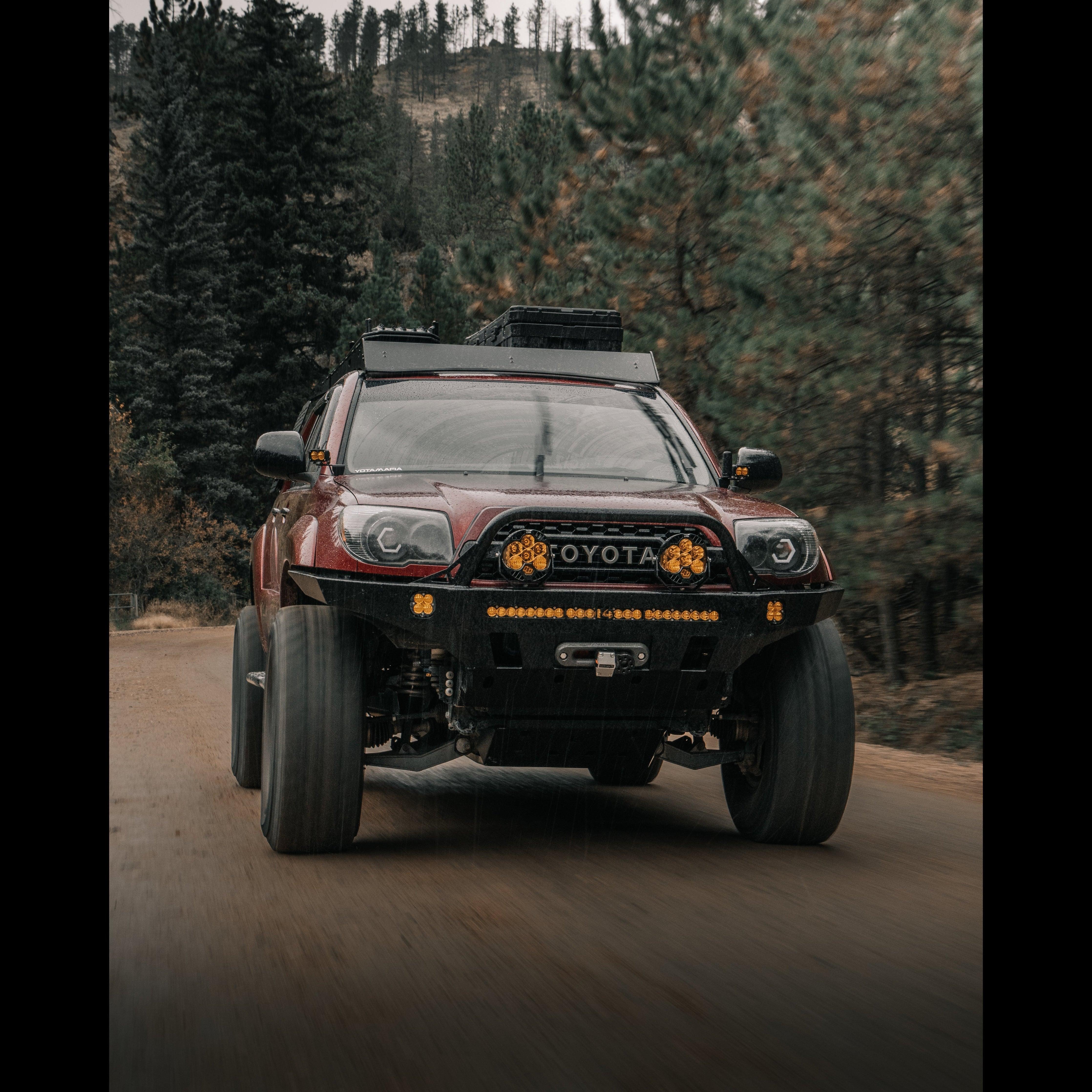 Toyota 4Runner with aftermarket bumper and off-road lights driving on a forest trail