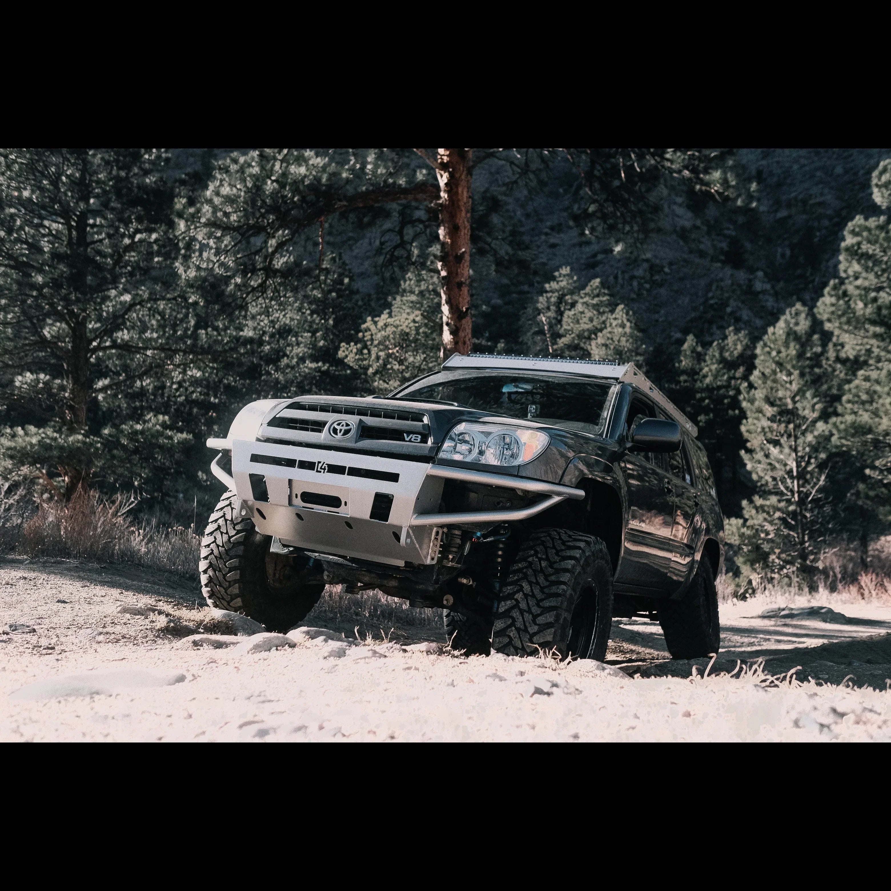 Toyota 4Runner with off-road bumper and lift kit parked on rugged dirt trail in forest