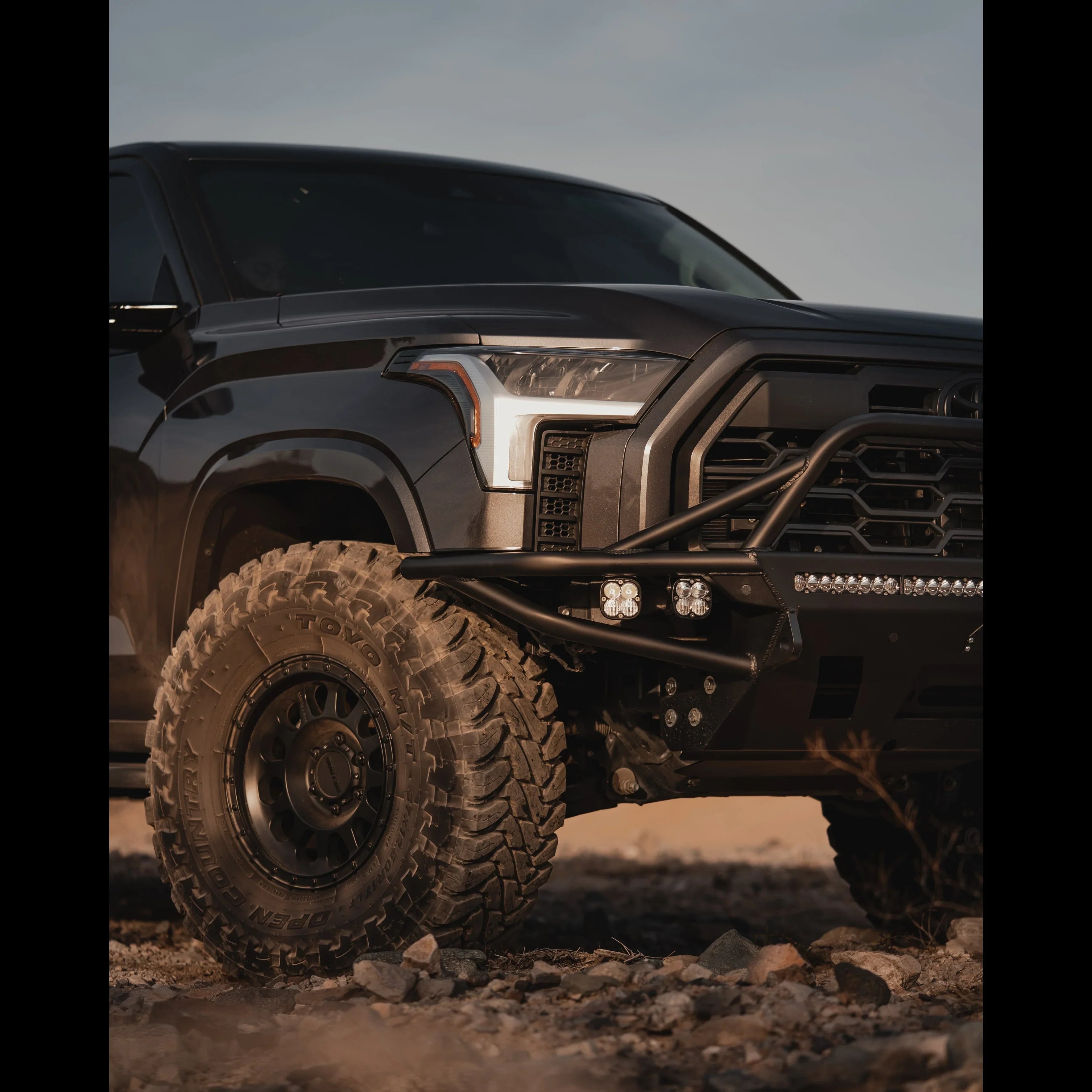Toyota Tundra front end with off-road bumper, LED lights, and large all-terrain tires on rocky terrain