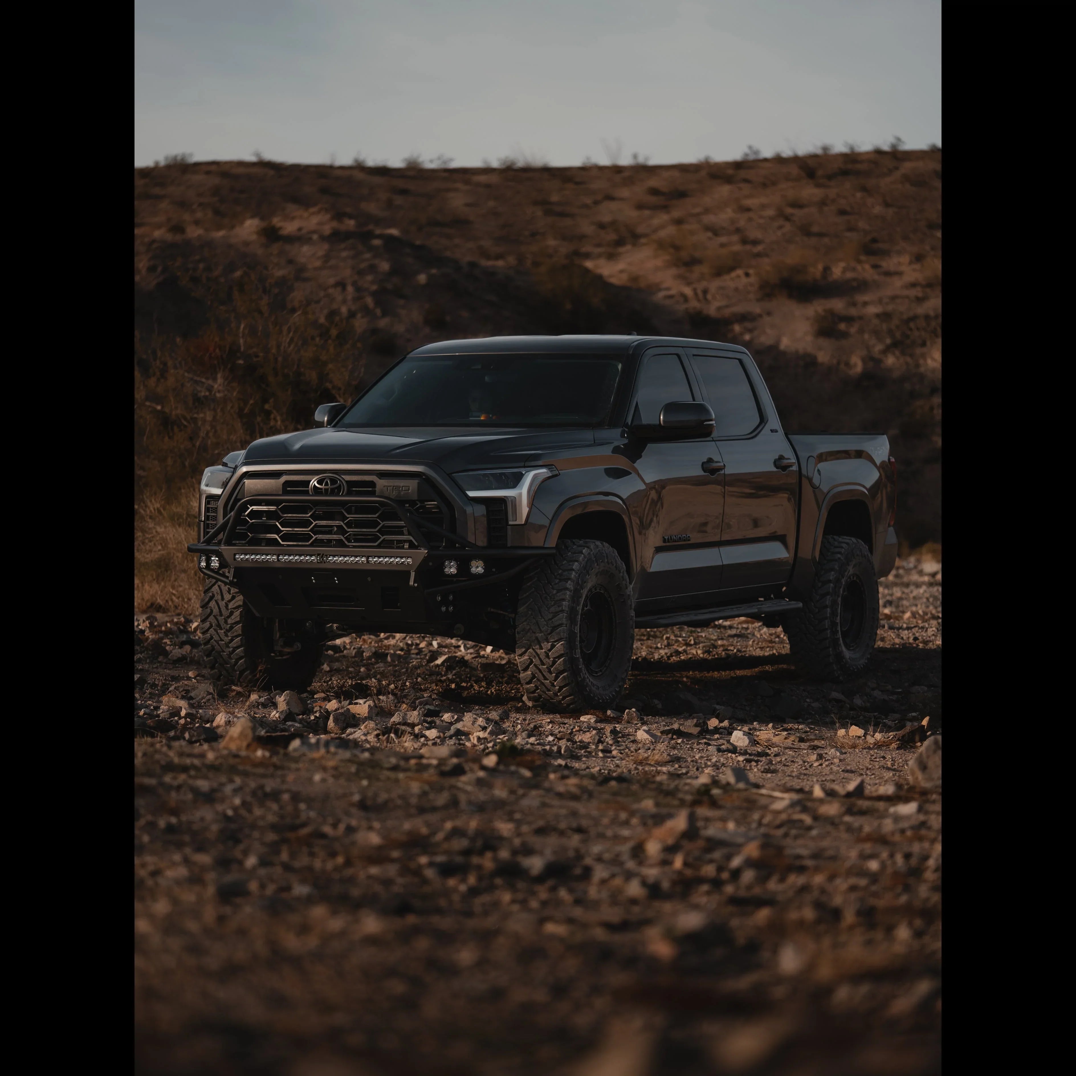 Black Toyota Tundra with off-road bumper and tires parked on rocky terrain outdoors.